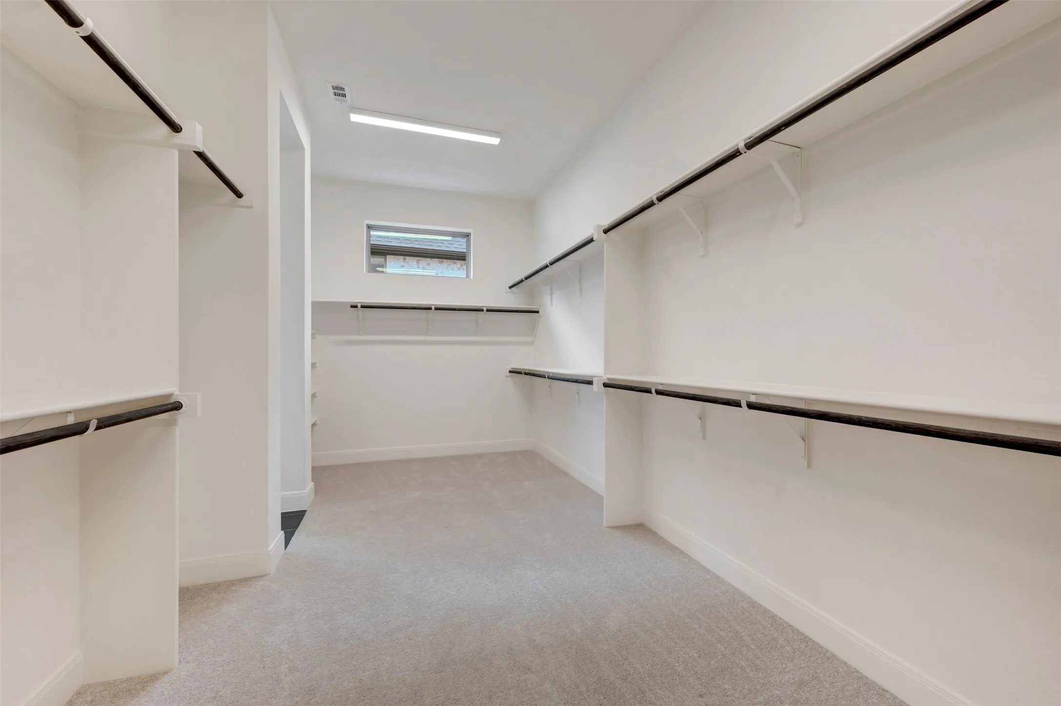 Expansive walk-in closet featuring light-colored carpeting, multiple hanging rods, extensive shelving, and a transom window for natural light
