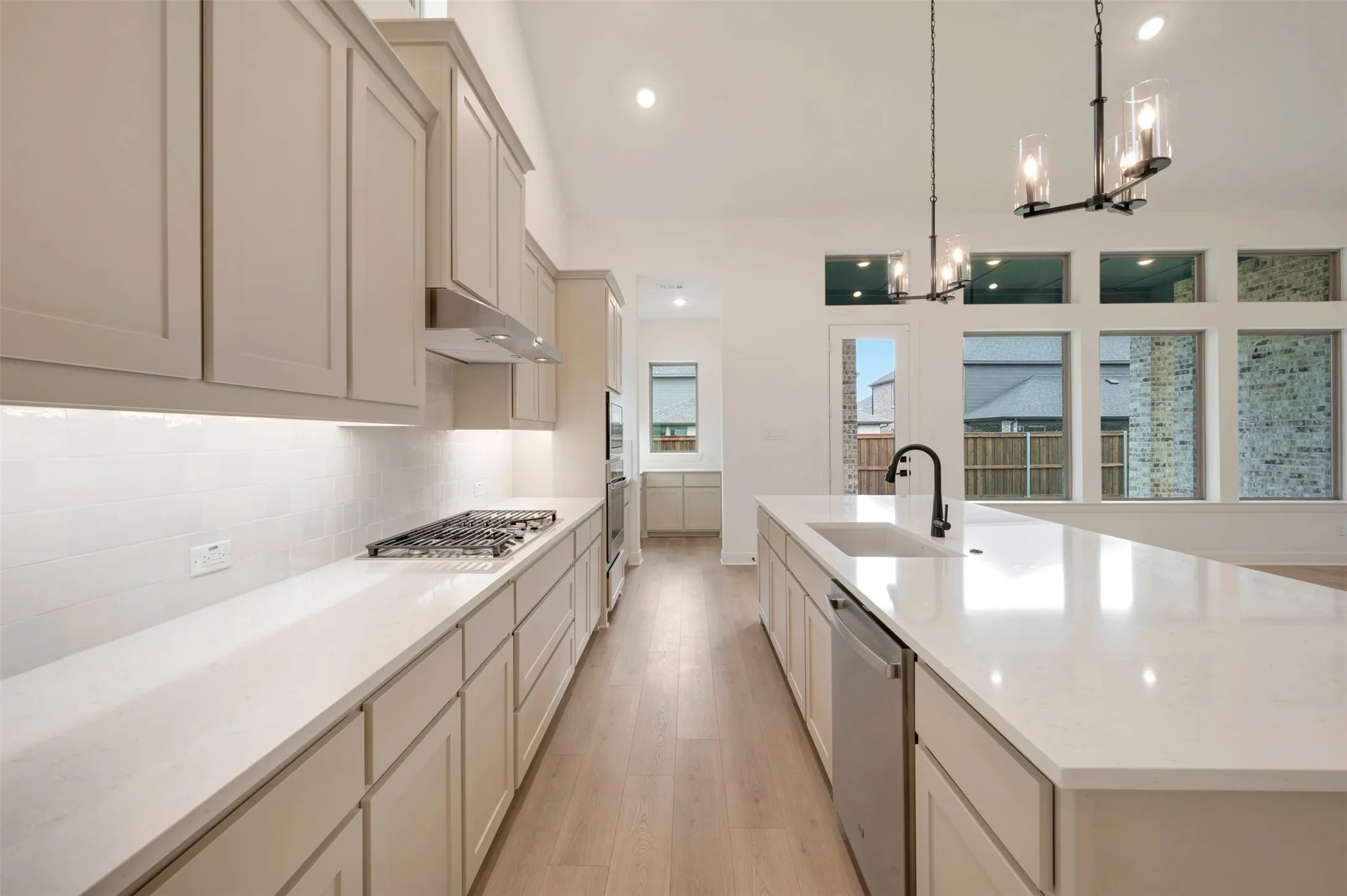 Chef's kitchen featuring custom cabinetry with integrated hardware, quartz countertops, a gas cooktop with stainless steel hood, and a large center island with waterfall edge