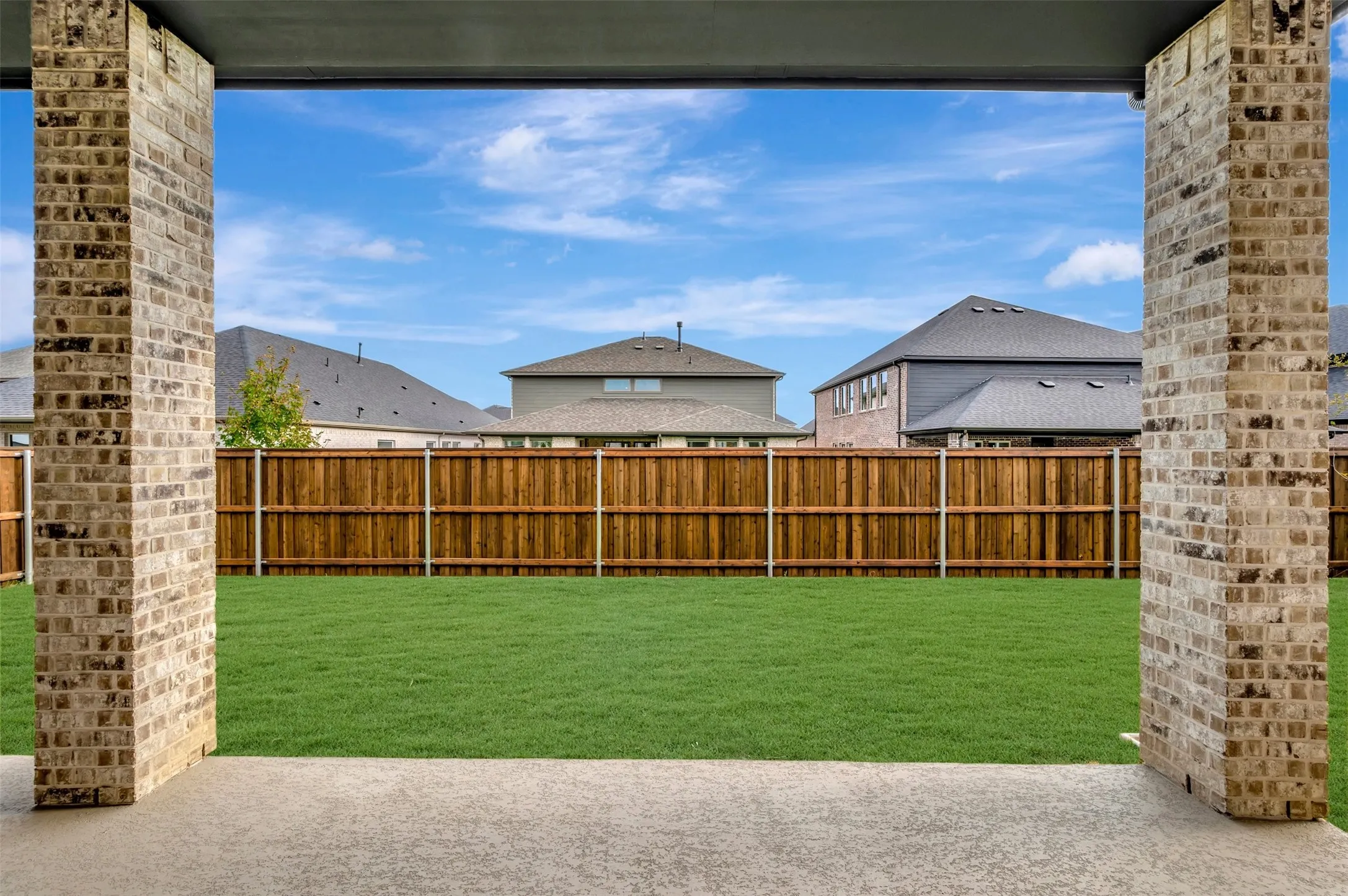 Expansive backyard featuring a manicured lawn, wood fencing, and a concrete patio with brick columns