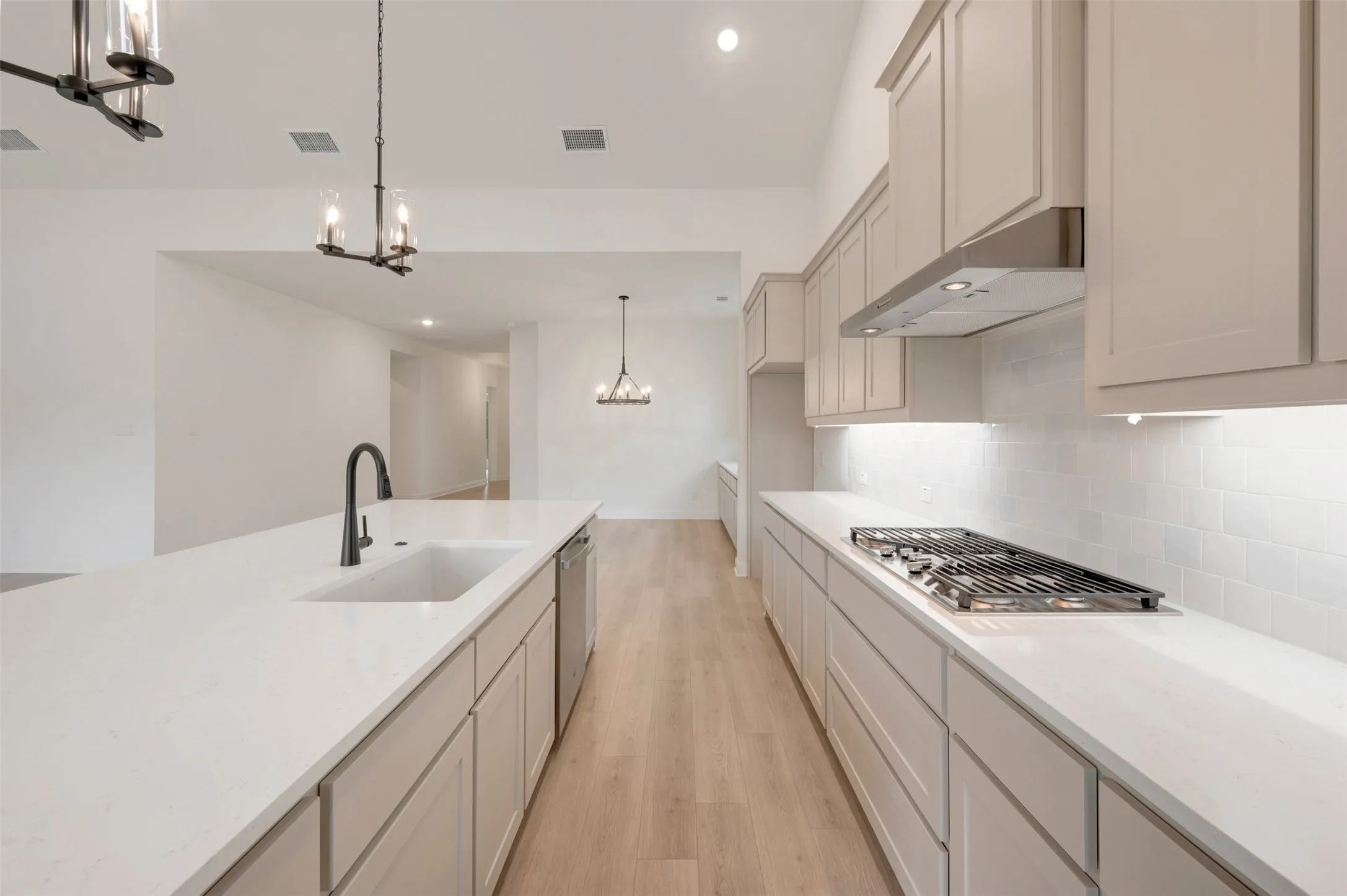 Expansive kitchen with an integrated gas cooktop, undercabinet lighting, wood-finish flooring, and a large central island with an undermount sink