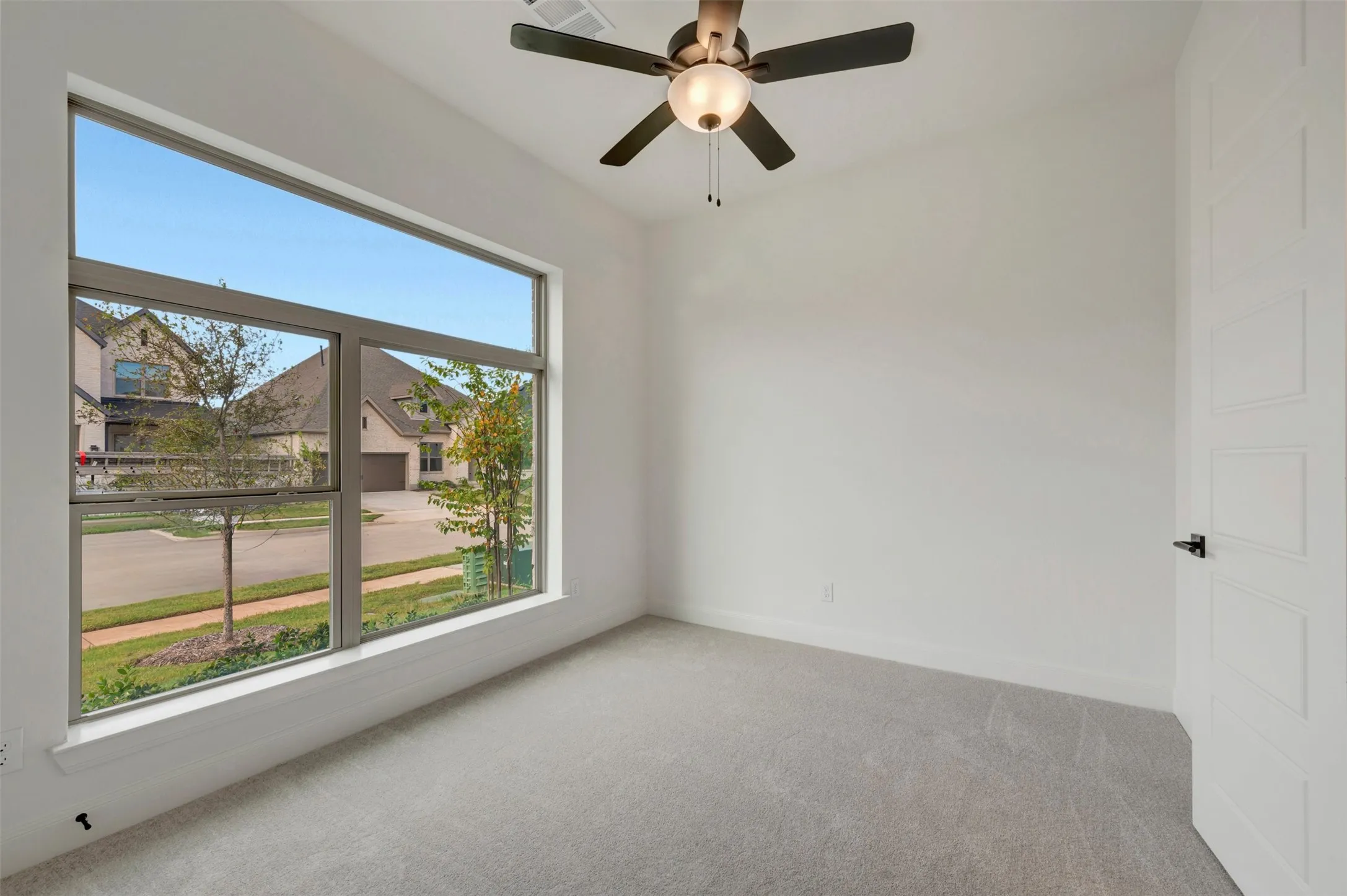 Expansive window offering abundant natural light, ceiling fan with integrated lighting, light-toned carpeting, and a contemporary paneled door with dark hardware
