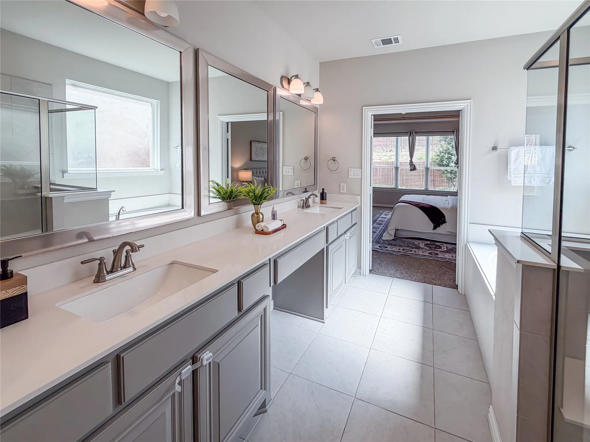 Bathroom featuring a dual vanity with light gray cabinetry and white countertops, a walk-in shower with clear glass enclosure, a built-in bathtub, and tile flooring
