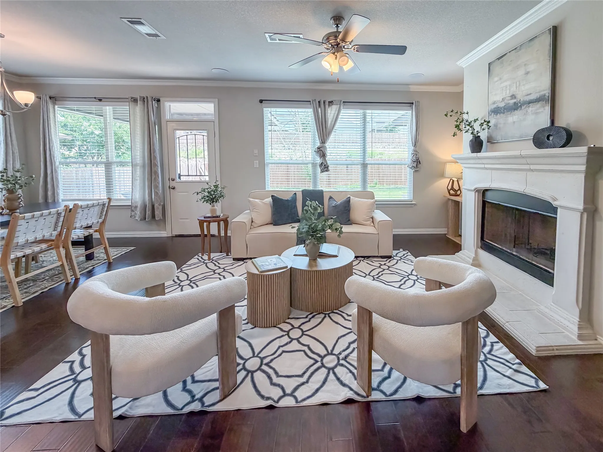 Spacious living area featuring rich wood-finish flooring, a decorative fireplace with a substantial mantel, and multiple windows providing ambient light