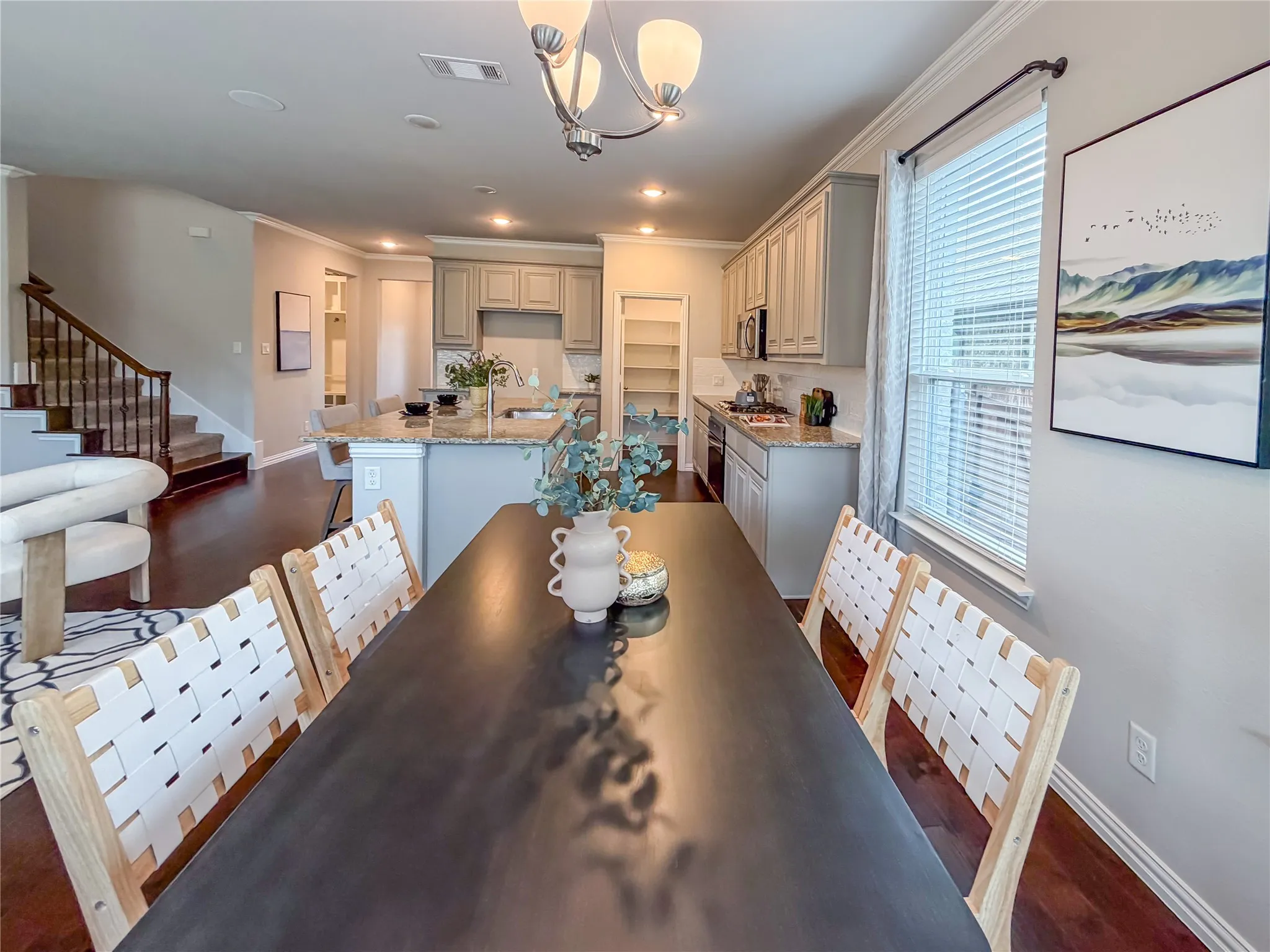 Open-concept living space featuring wood-finish flooring, a kitchen island with granite-style countertop, recessed lighting, and a staircase with wood newel posts and iron balusters