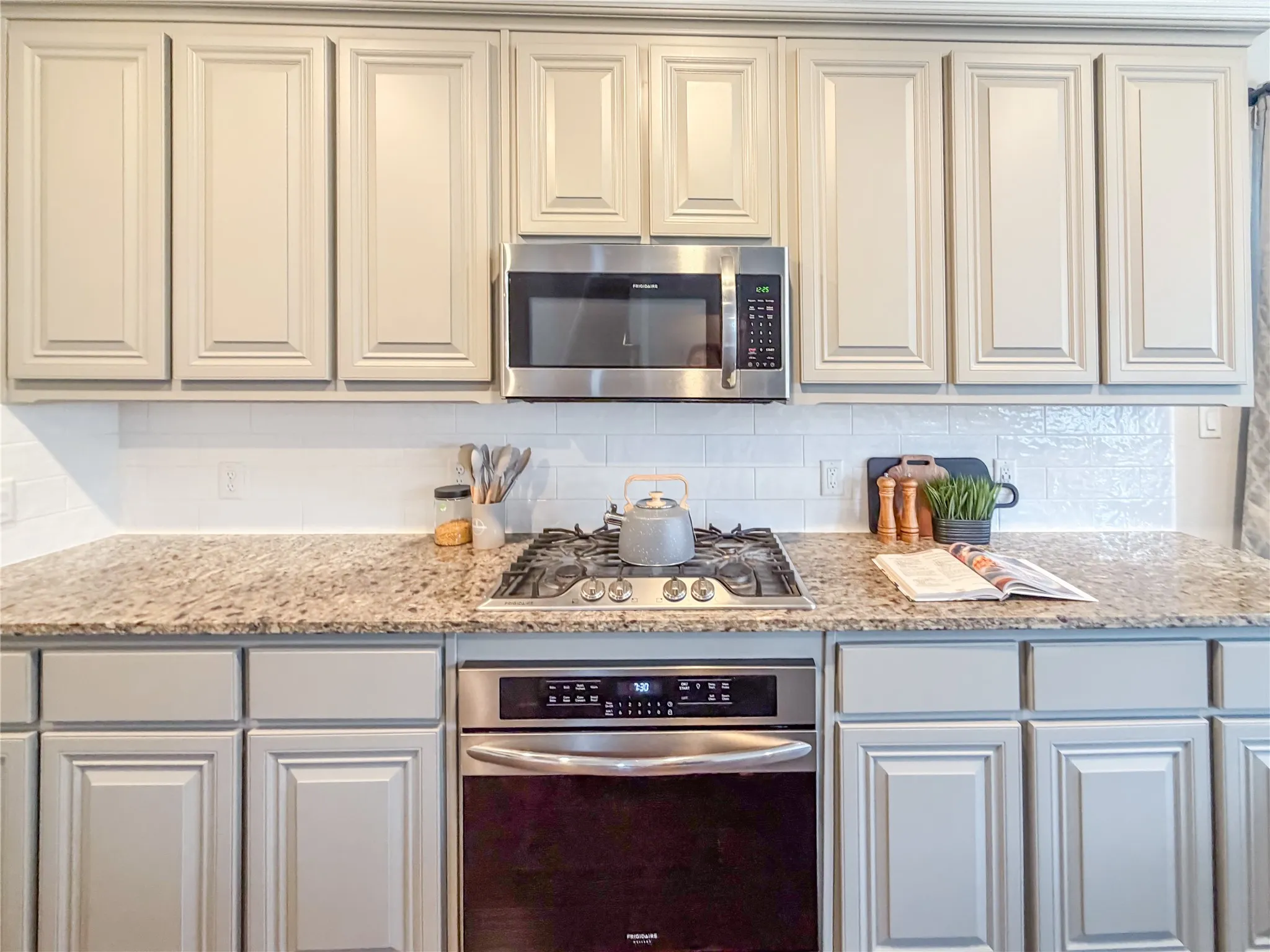 Kitchen featuring light-toned cabinetry, granite-style countertops, stainless steel appliances, a built-in microwave, and a subway tile backsplash