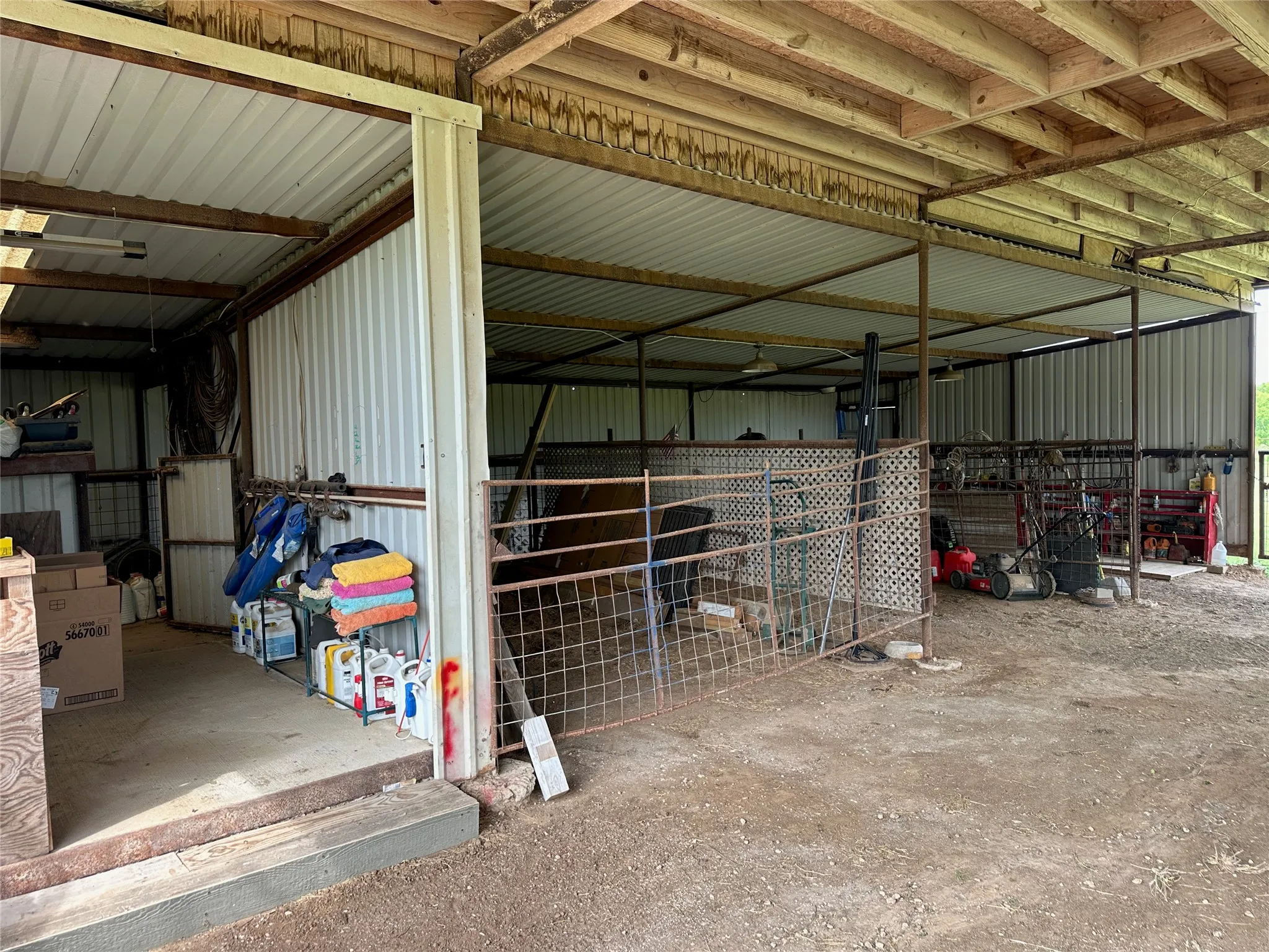 Multi-purpose metal outbuilding with a corrugated metal roof, exposed wood joists, and a partial concrete floor