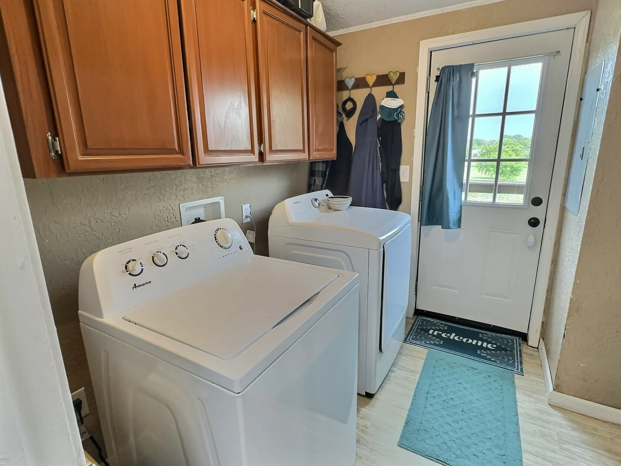 Dedicated laundry area featuring wood-finish flooring, overhead cabinetry, and a white exterior door with an inset window