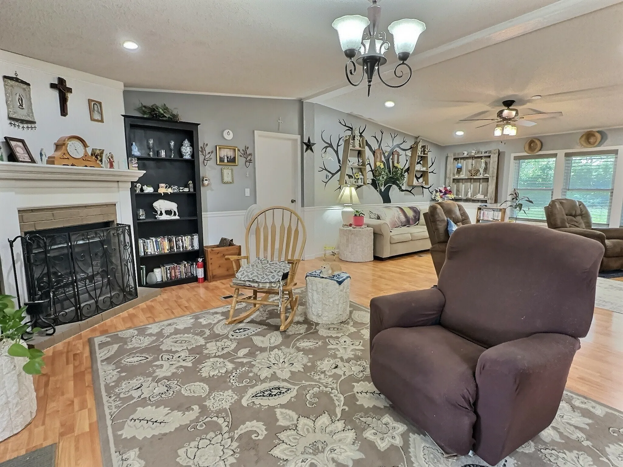 Spacious living area featuring wood-finish flooring, a fireplace with a white mantel, and a built-in black bookcase