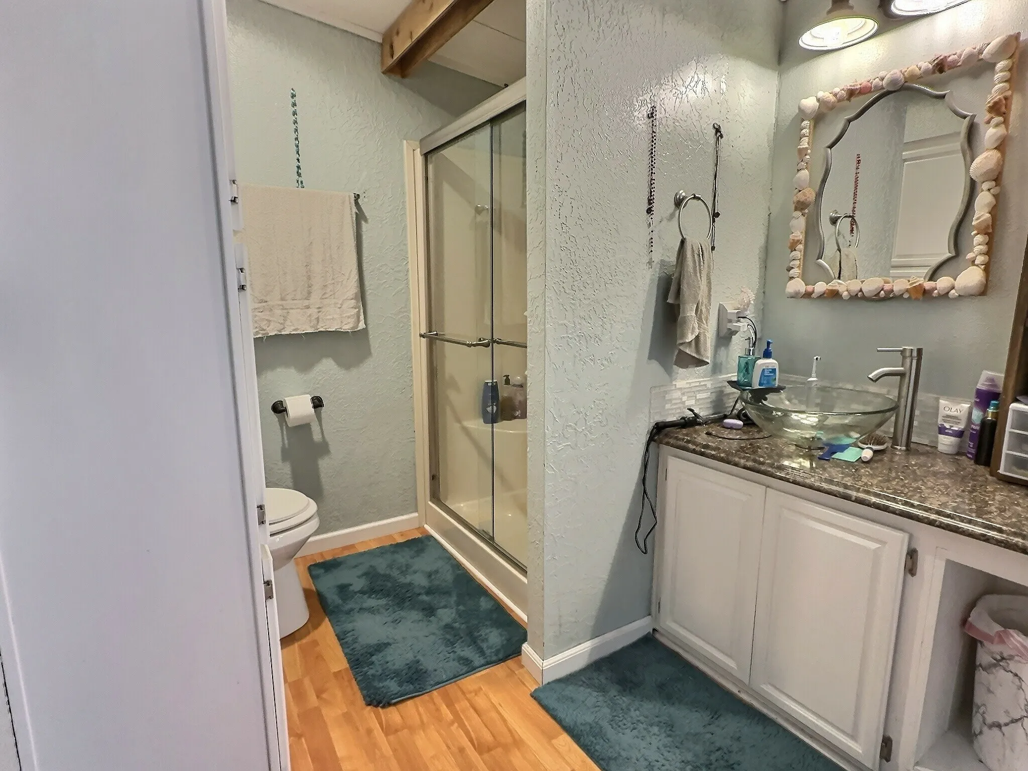 Bathroom featuring a walk-in shower with clear glass enclosure, wood-finish flooring, a toilet, a vanity with a granite-style countertop, and a vessel sink with a contemporary faucet
