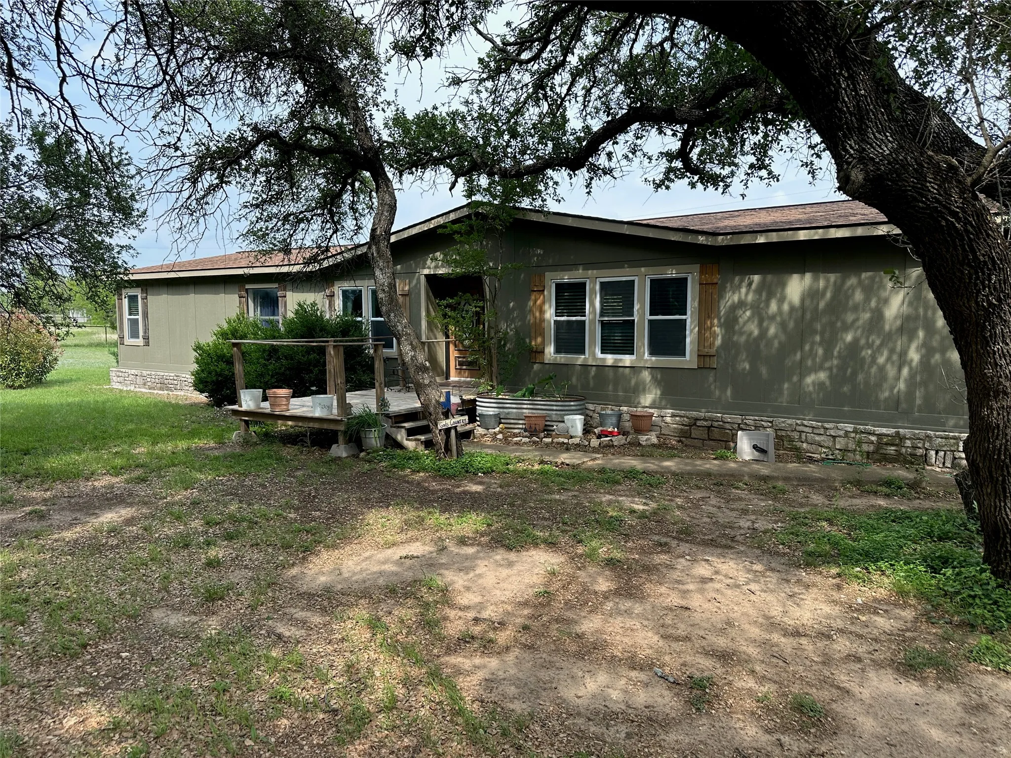 Ranch-style residence featuring a weathered wood deck, mature shade trees, and a stone foundation