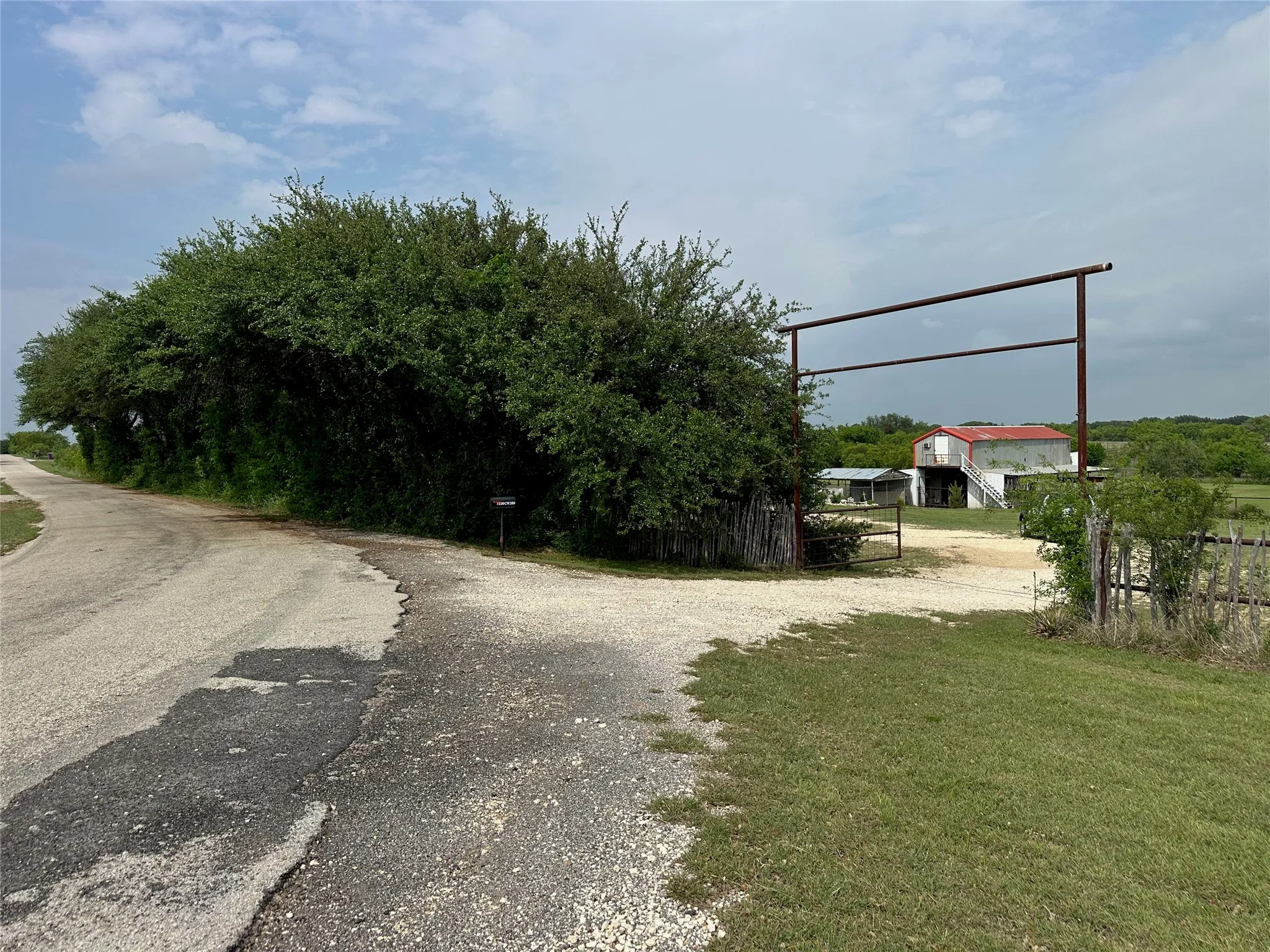 Gravel driveway entrance with an overhead metal frame and a wooden fence