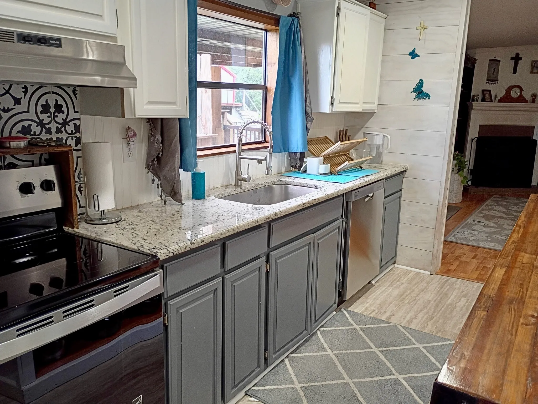 Kitchen area featuring granite-style countertops, stainless steel appliances, a tile backsplash with a decorative pattern, and grey base cabinetry with white upper cabinets