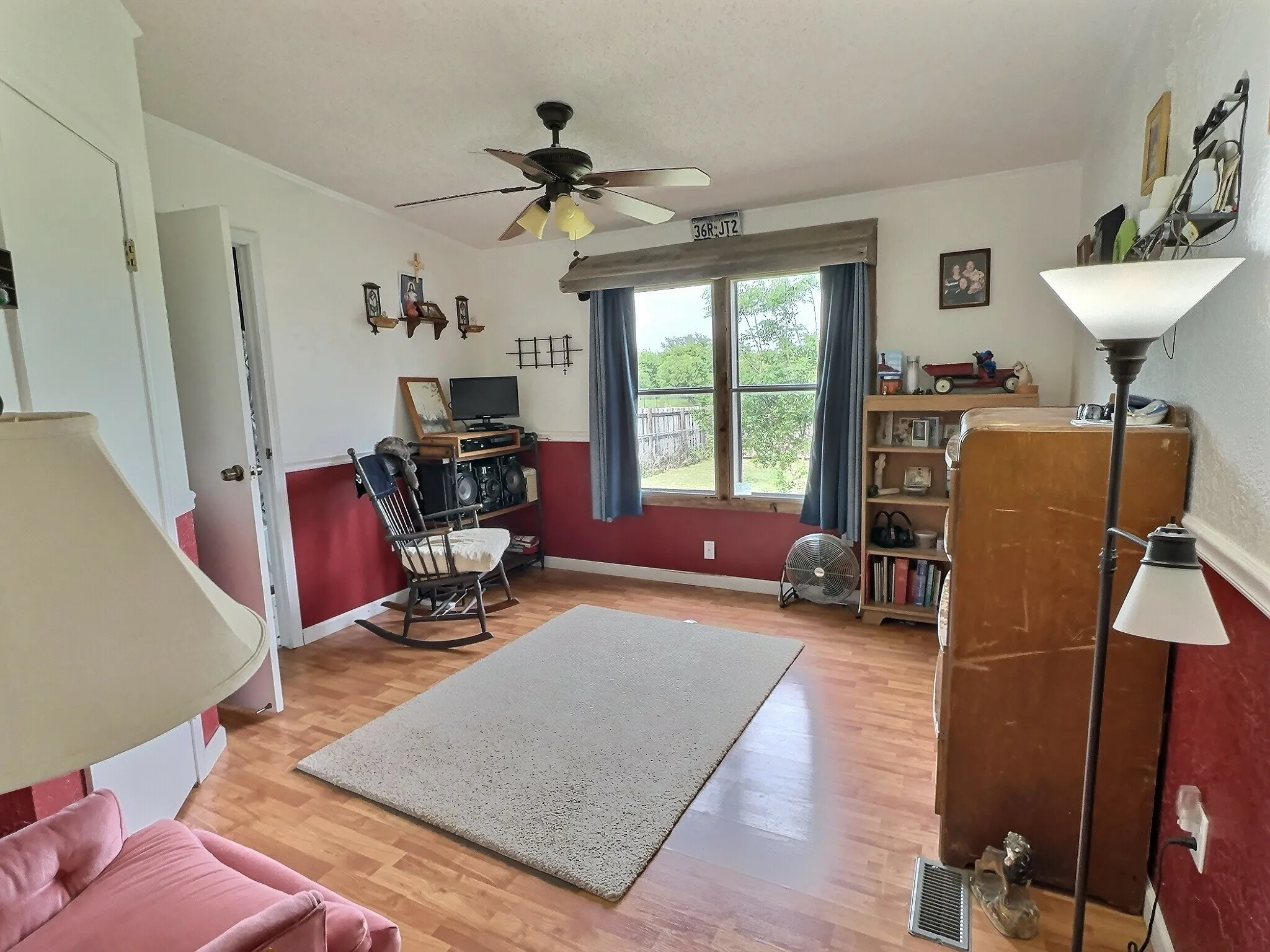 Room featuring wood-finish flooring, a ceiling fan with integrated lighting, and a large window with blue drapes