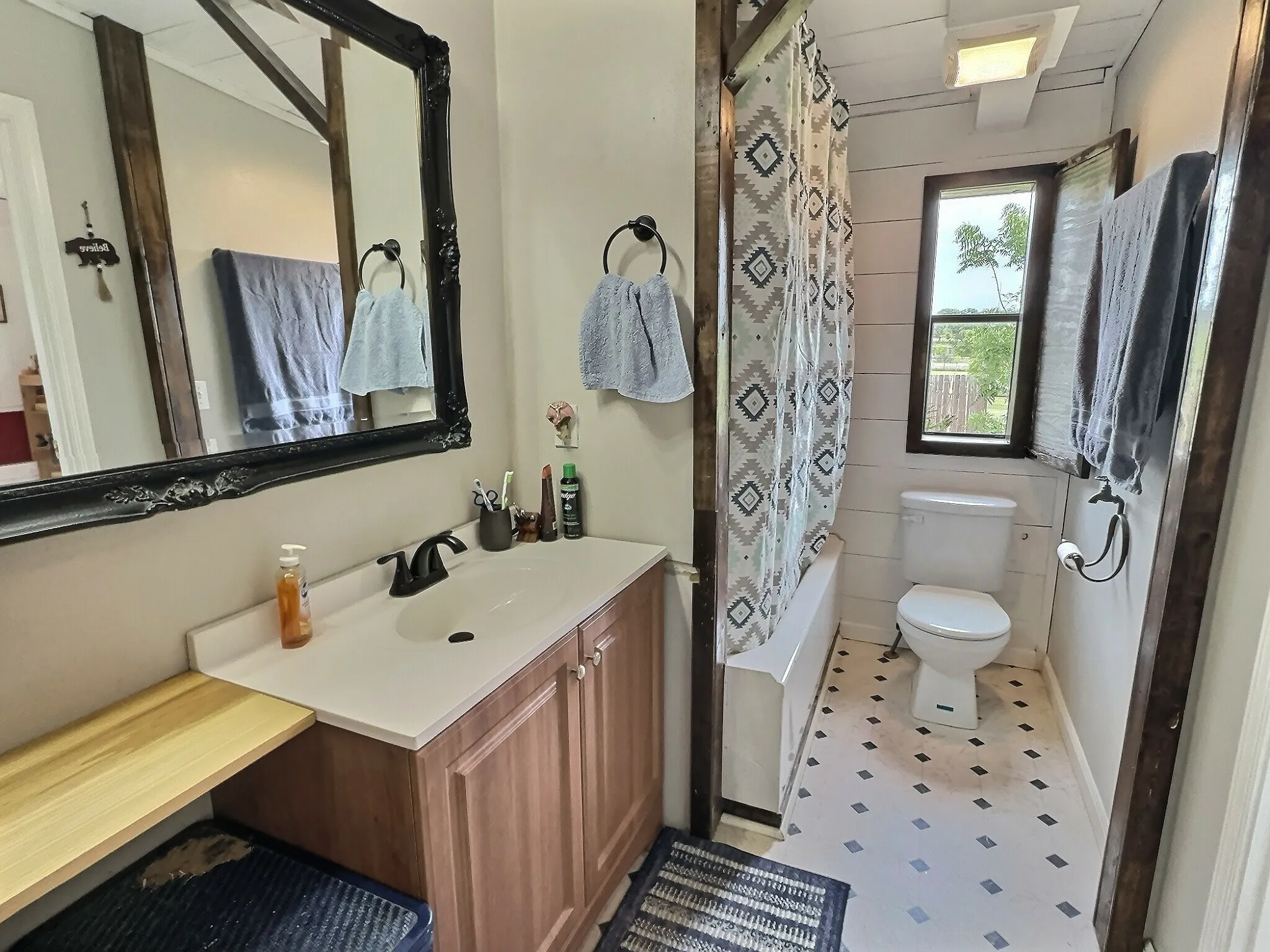 Bathroom featuring a single vanity with a white countertop, wood-finish cabinetry, and a black-framed mirror