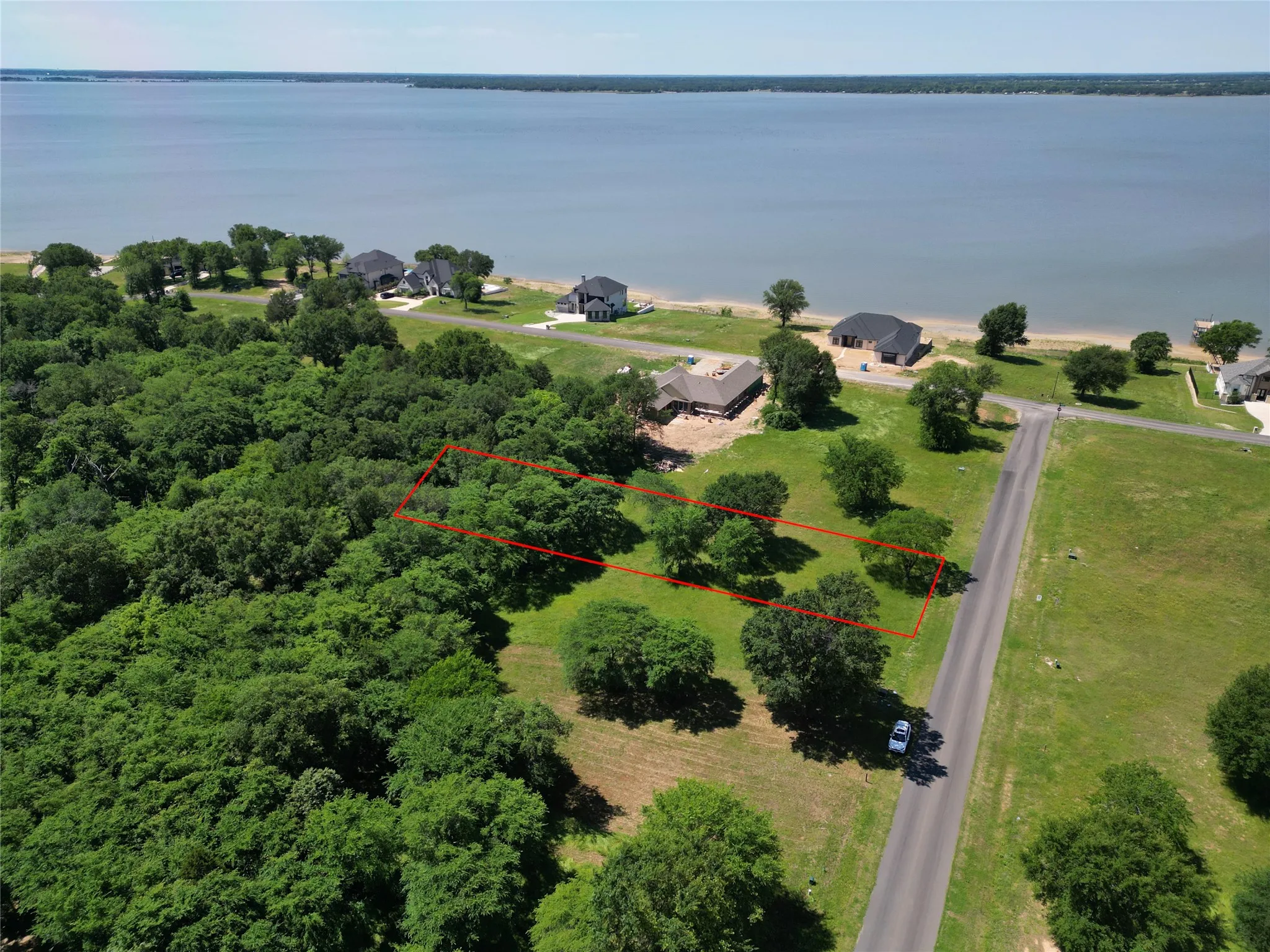 Expansive wooded lot with partial clearing, featuring mature trees and a paved road frontage