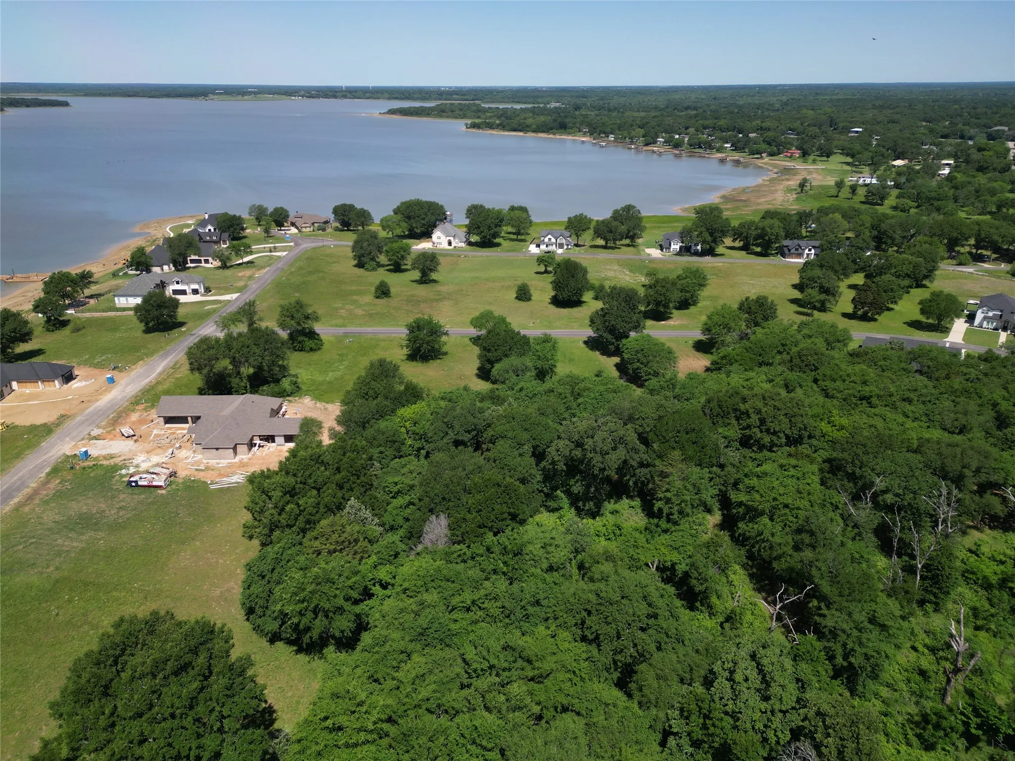 Expansive aerial overview showcasing a large body of water, residential properties with green lawns, and dense wooded areas