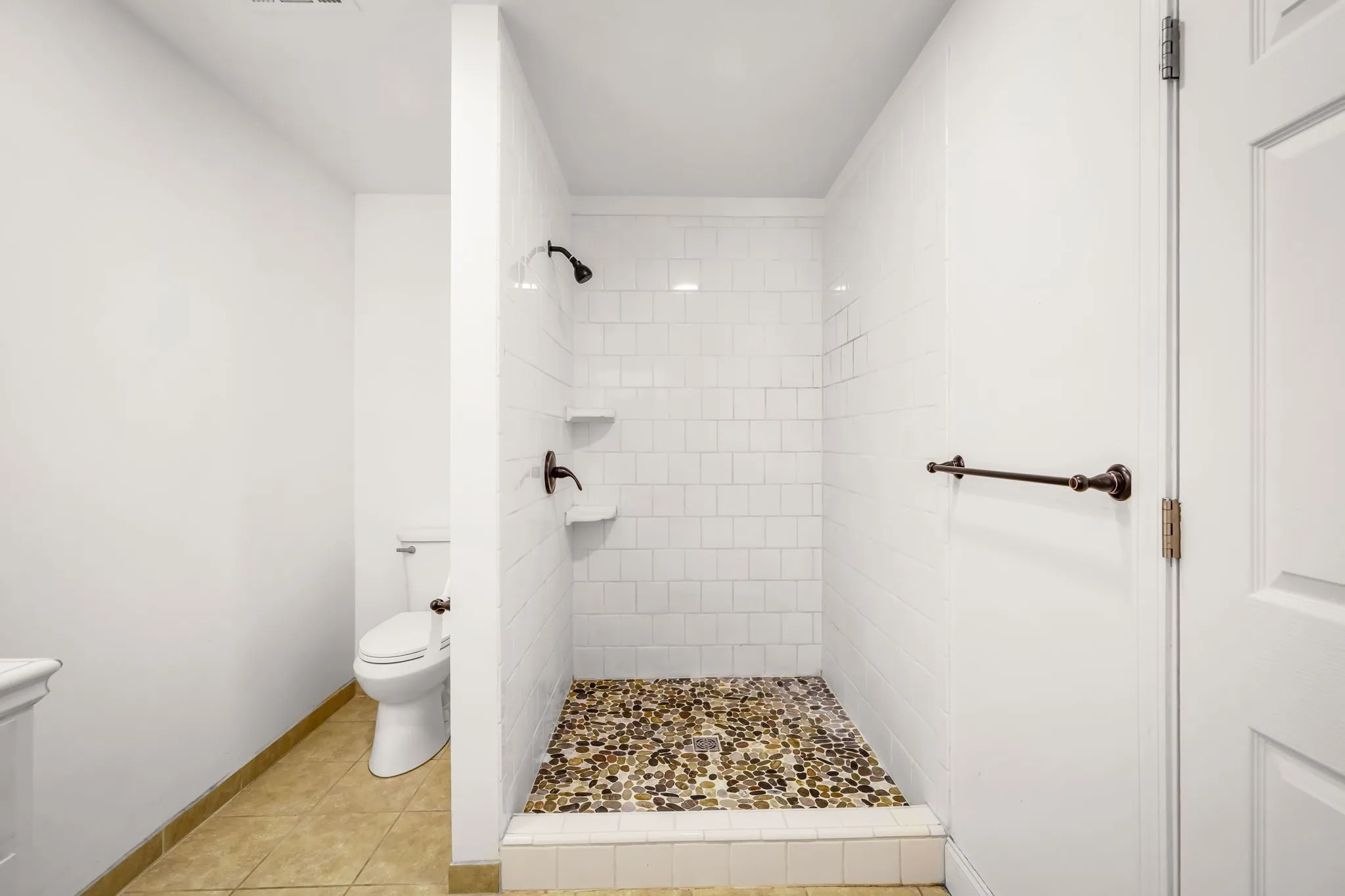Walk-in shower featuring pebble stone floor, white subway tile surround, and matte black fixtures