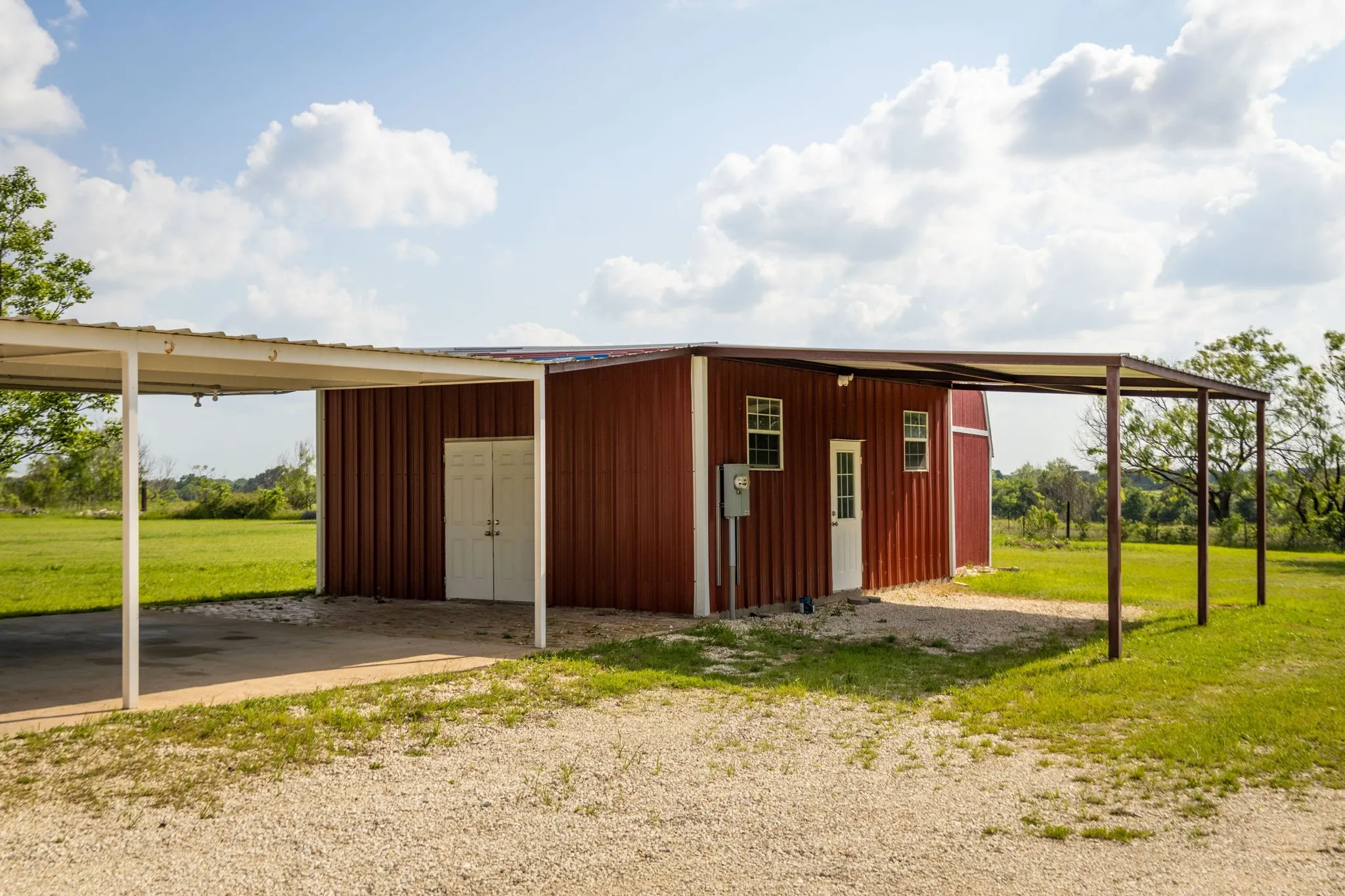 Red metal building featuring multiple windows and two covered carport areas
