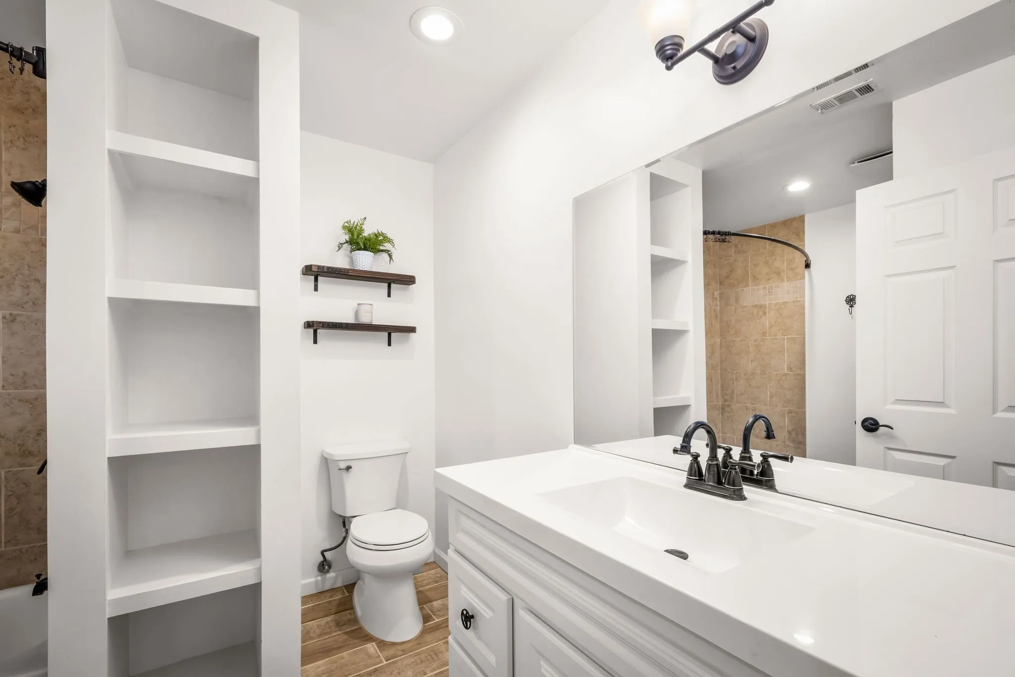 Bathroom featuring a white vanity with integrated sink, a large wall-mounted mirror, recessed lighting, and a bathtub with tile surround