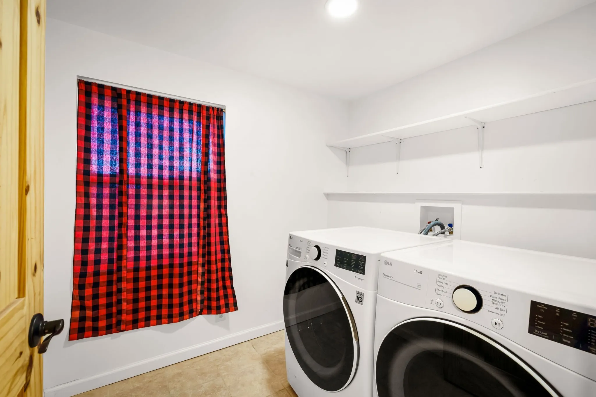 Dedicated laundry space featuring a window, built-in shelving, and light-toned tile flooring