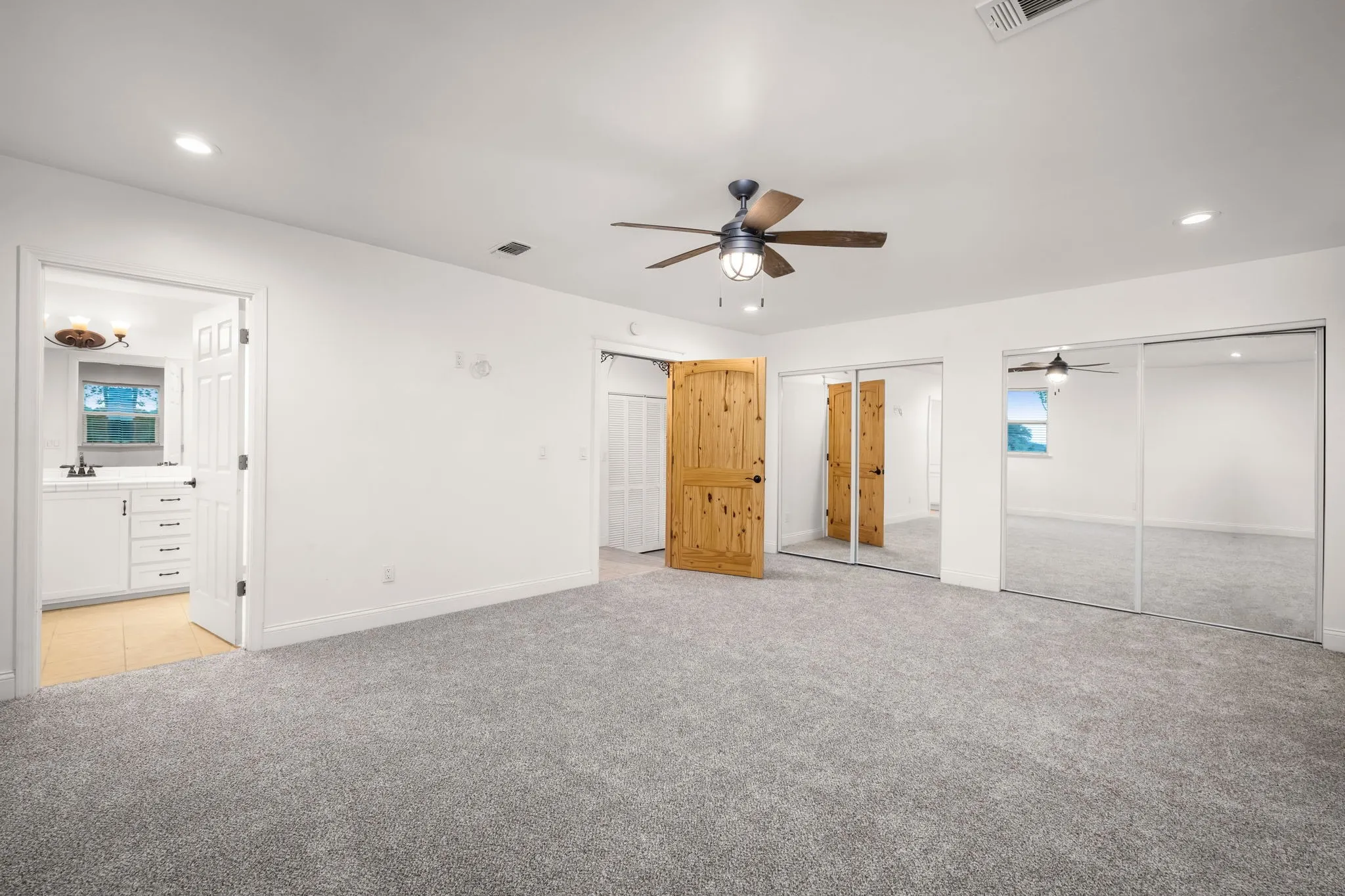 Spacious room featuring gray carpet flooring, a ceiling fan with integrated lighting, recessed lighting, and mirrored sliding closet doors