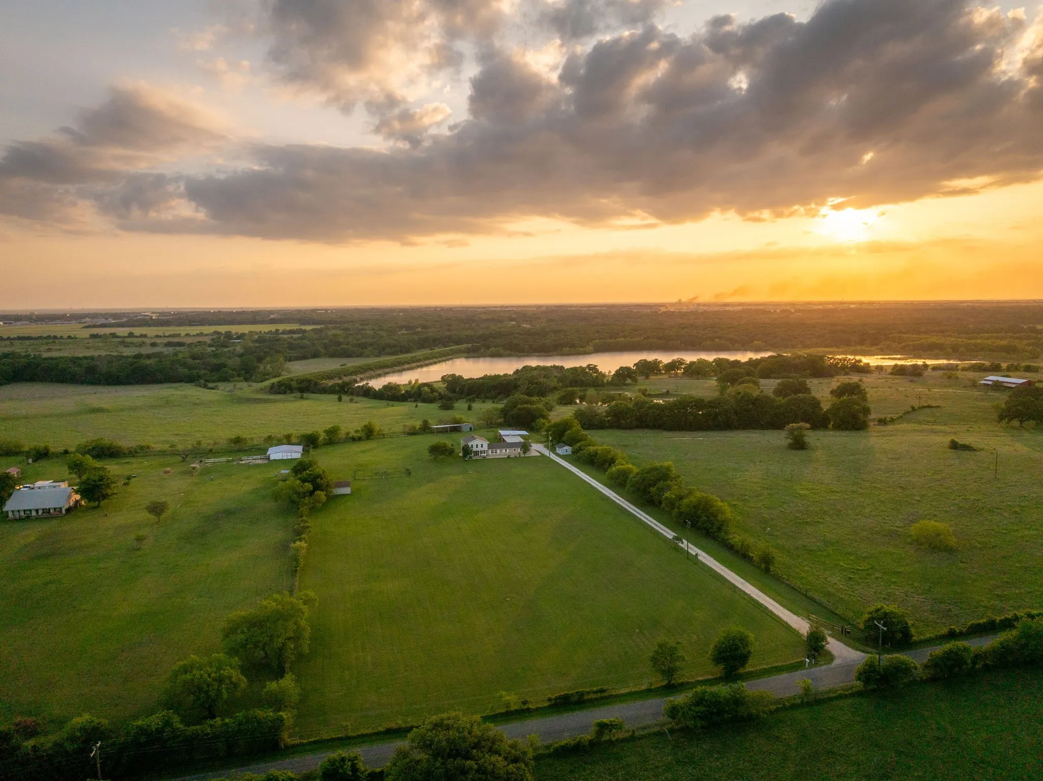 Expansive green acreage with multiple structures, a private drive, and mature trees, offering distant water views
