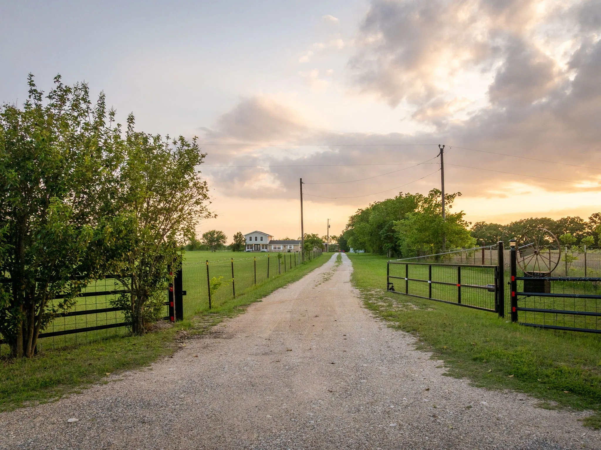 Gravel driveway leading to a residence, bordered by green grass and a wire fence
