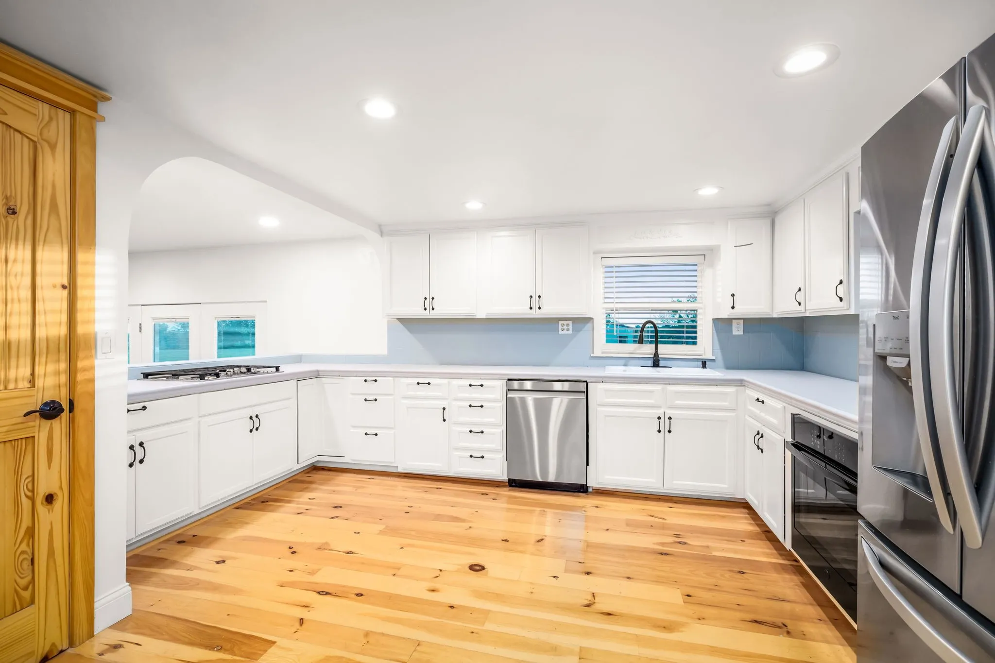 Kitchen featuring white cabinetry, light-tone wood flooring, stainless steel appliances, a black faucet, and a light blue backsplash