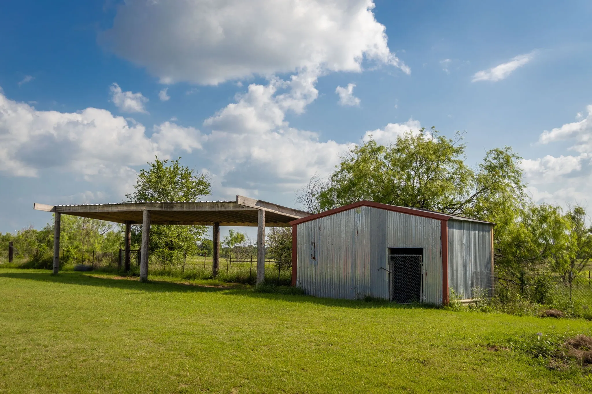 Galvanized metal utility building with red trim, featuring a chain-link door