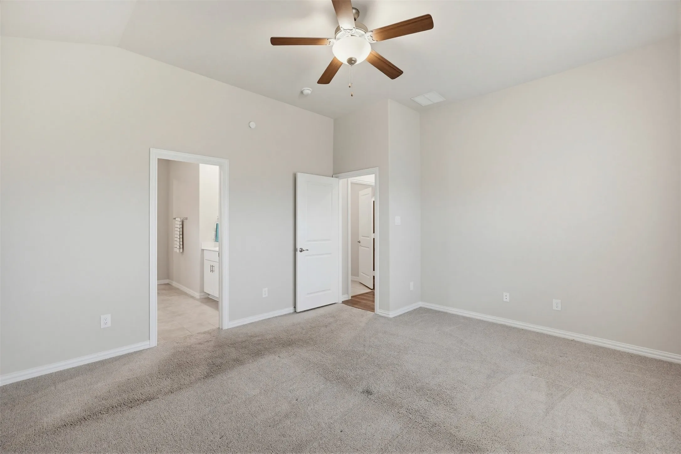 Spacious room featuring vaulted ceilings, light gray wall paint, and plush carpet flooring