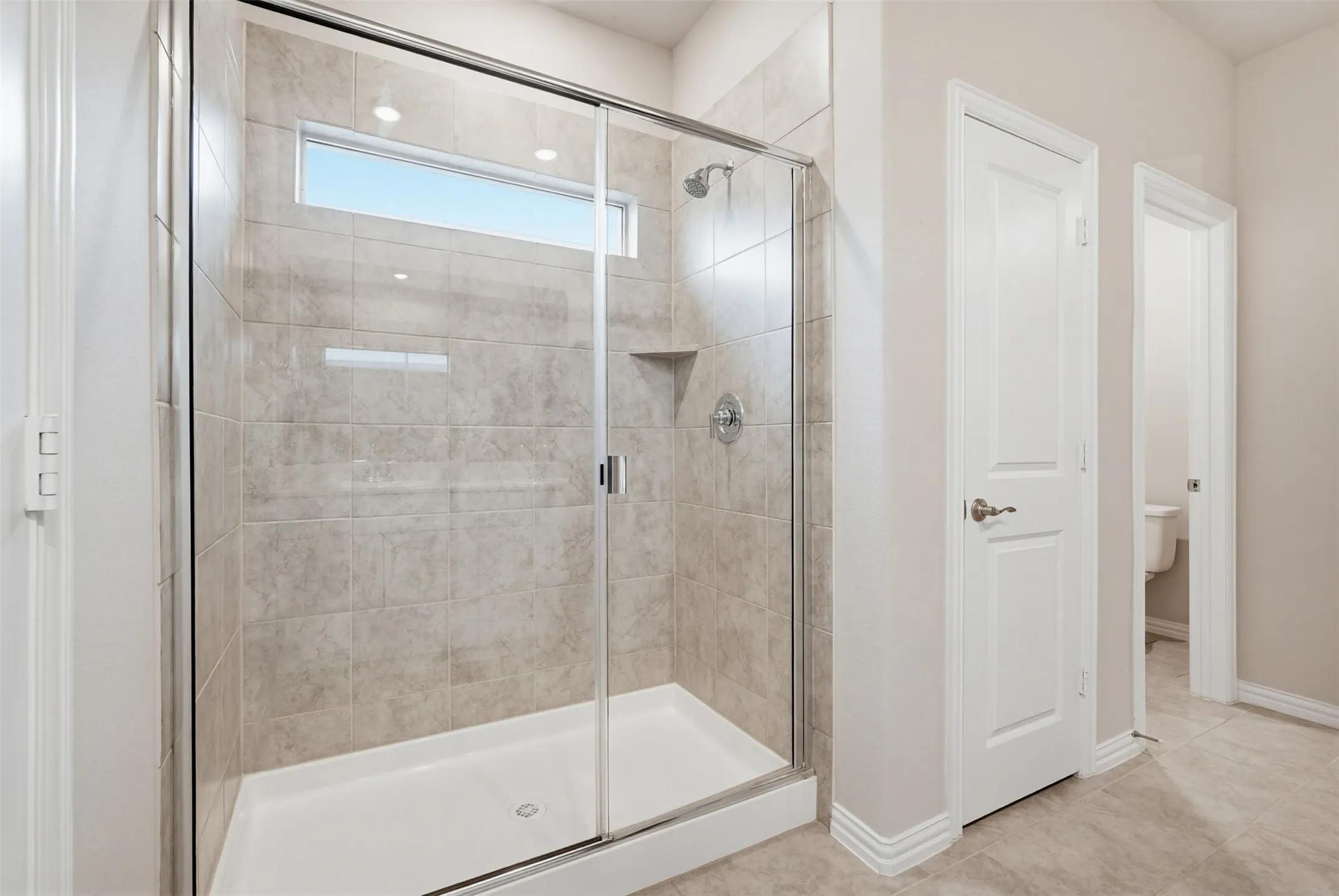 Spacious shower enclosure featuring light-toned tilework and a glass sliding door
