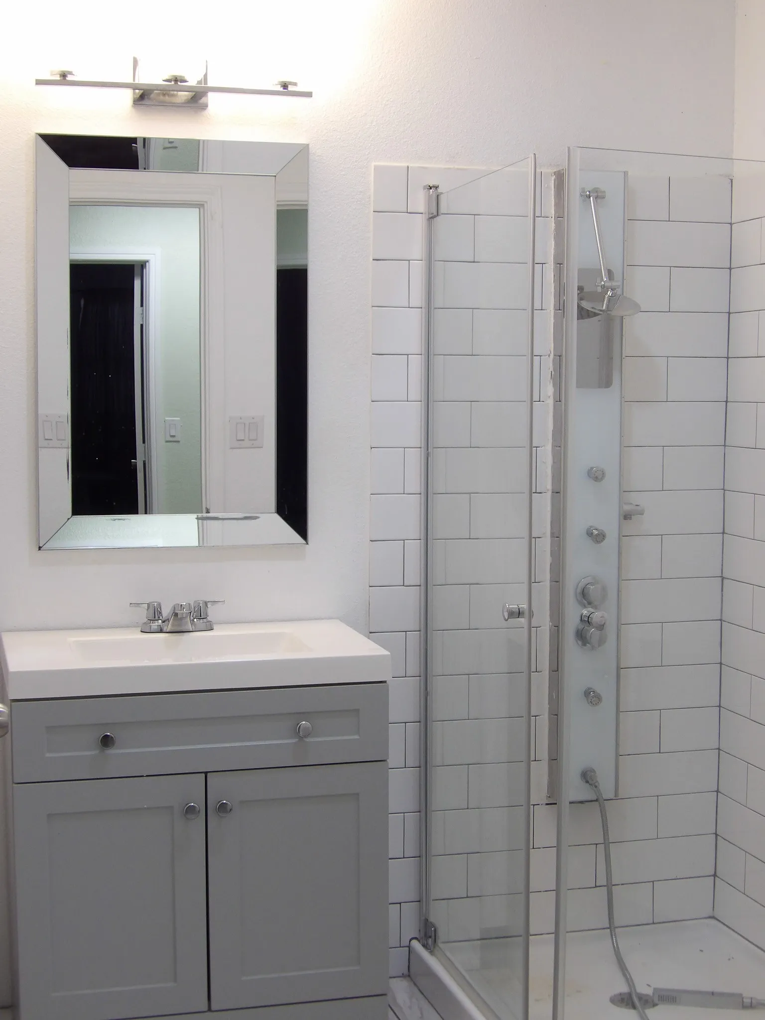 Bathroom featuring a gray shaker-style vanity with an integrated white sink, a framed mirror, and a modern shower system within a glass enclosure with subway tile surround