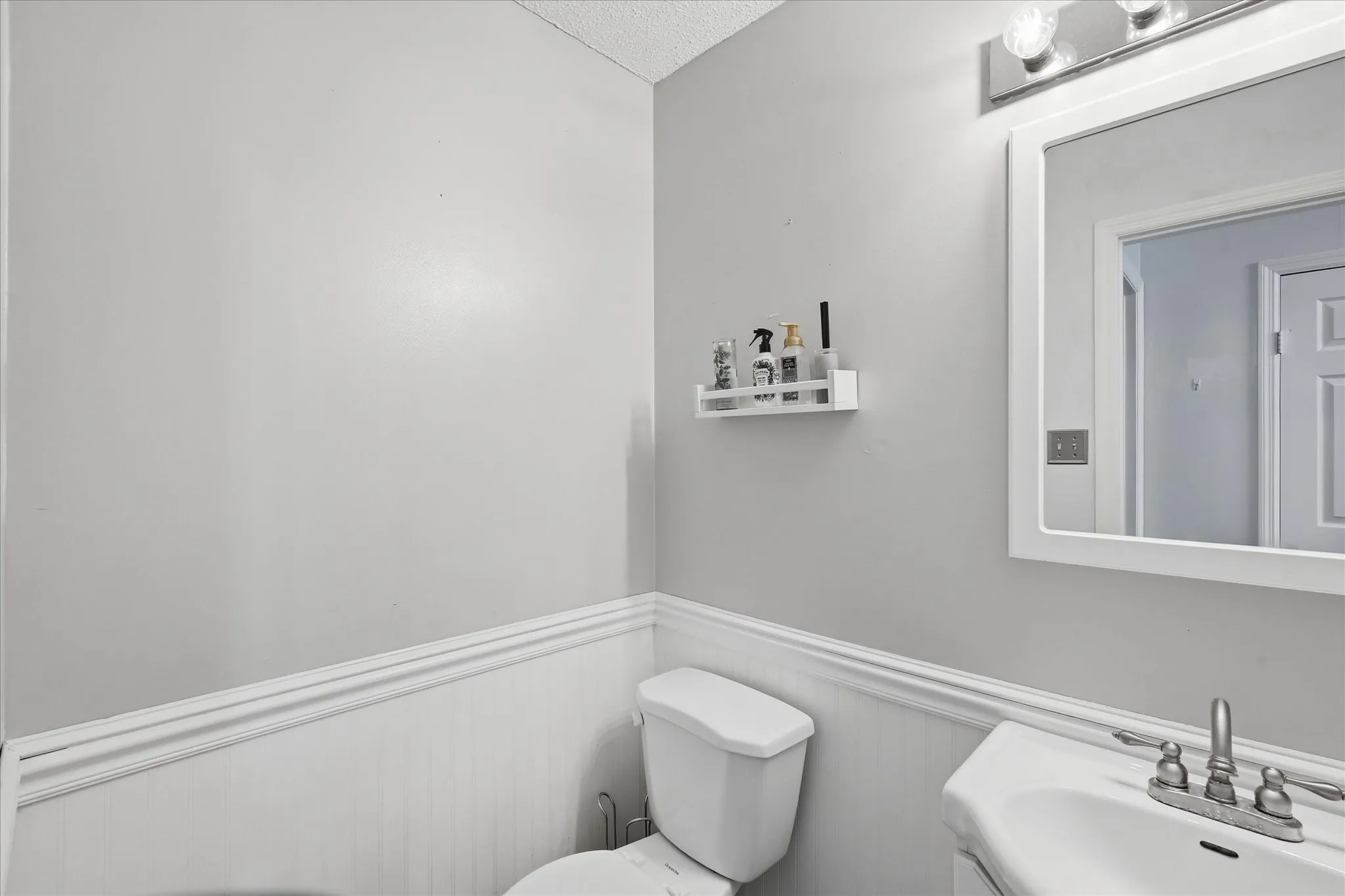 Pedestal sink with chrome faucet, complemented by a framed mirror and overhead vanity lighting