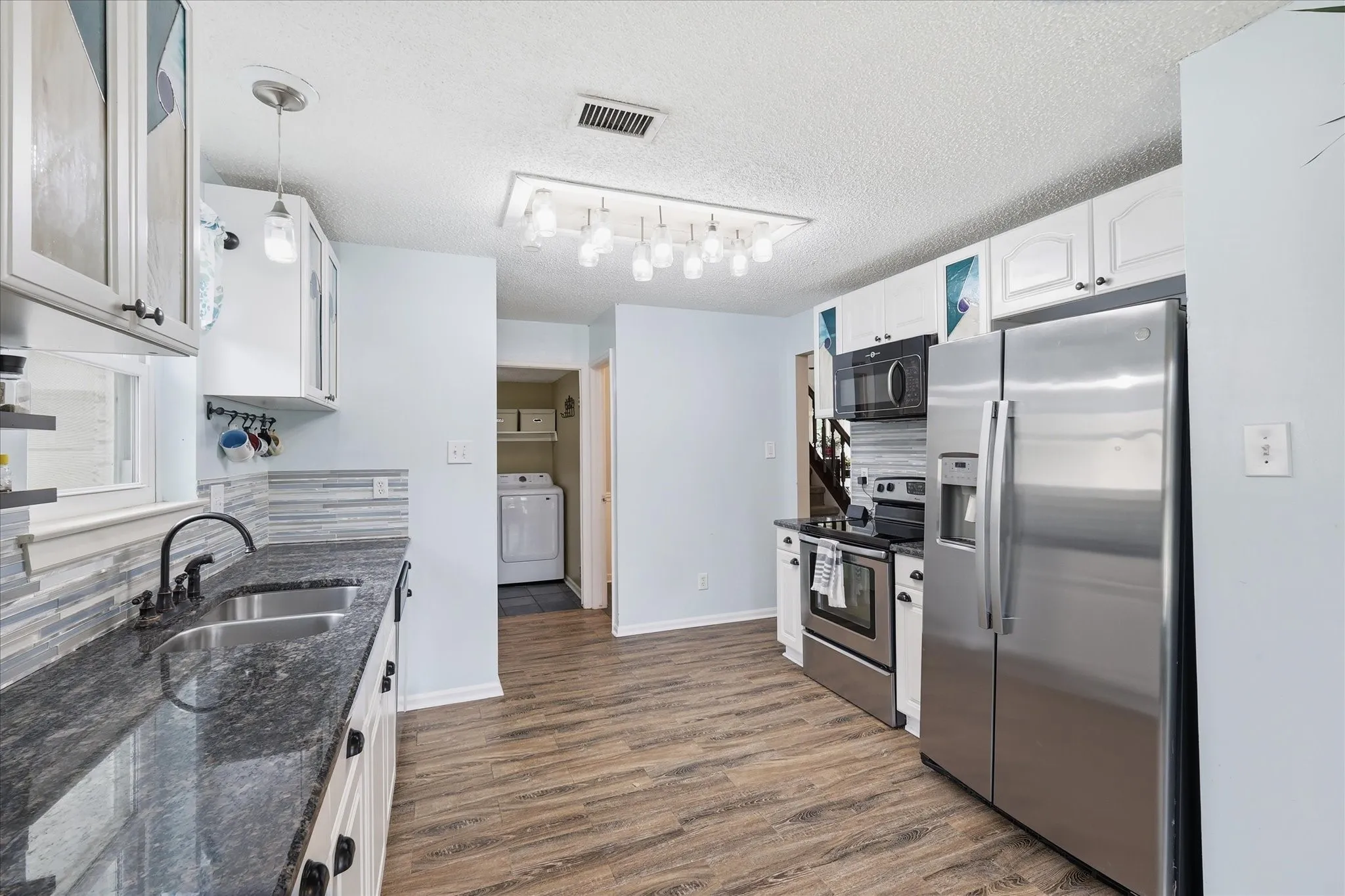 Modern kitchen featuring wood-finish flooring, white cabinetry, dark countertops, a stainless steel side-by-side refrigerator, and a coordinating range and microwave