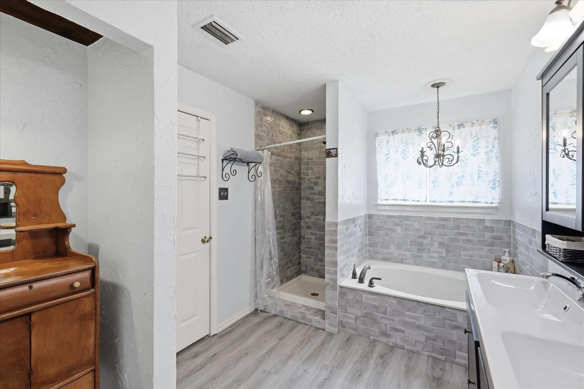 Bathroom featuring a walk-in shower with subway tile surround, a built-in bathtub with subway tile wainscoting, and a vanity with an integrated sink