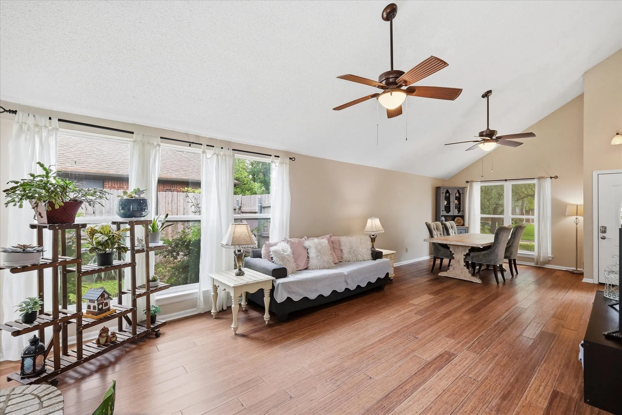 Spacious open-concept living area featuring wood-finish flooring, vaulted ceilings, and multiple windows