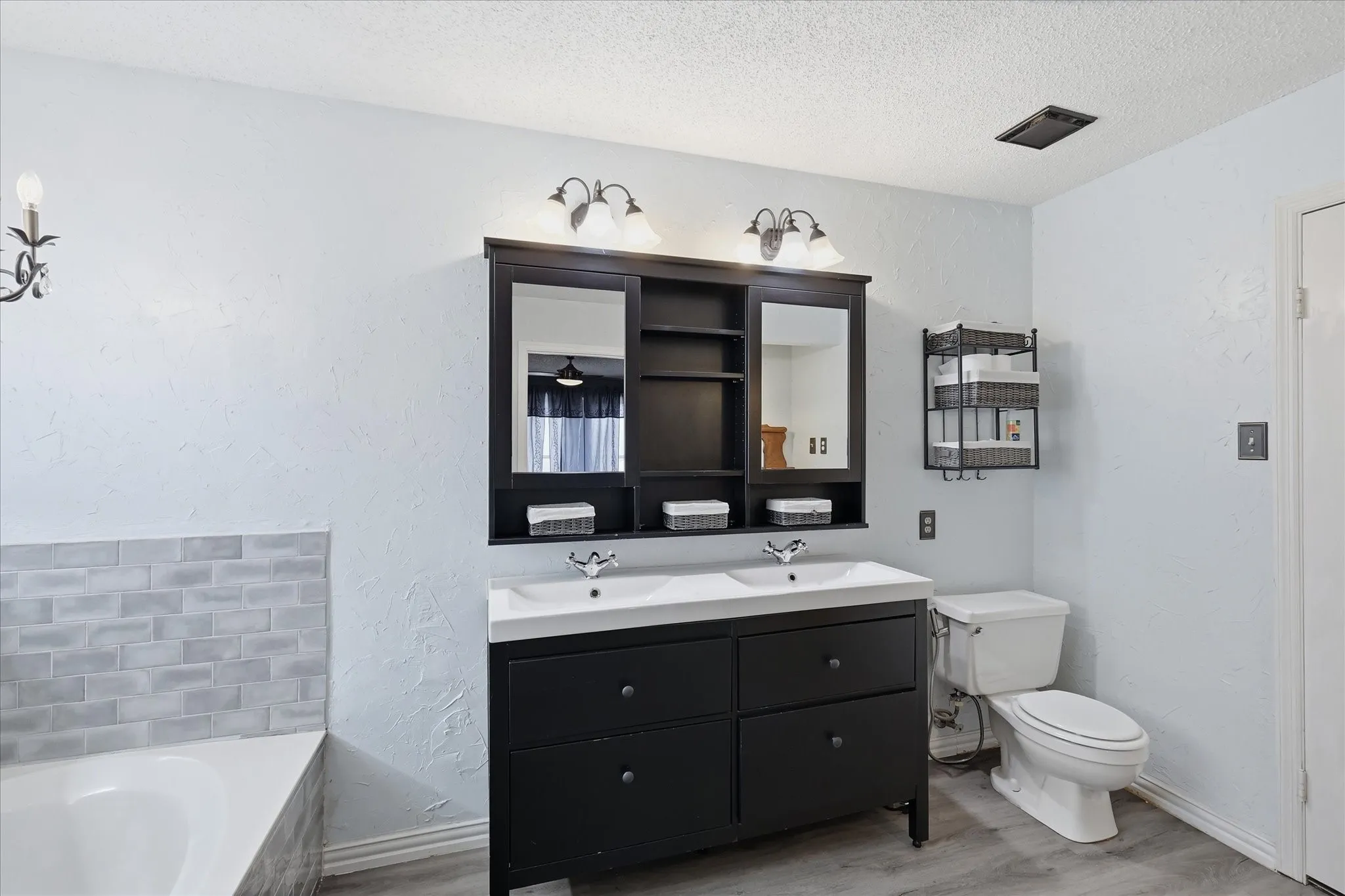 Bathroom featuring a double vanity with dark cabinetry and dual sinks, complemented by an overhead mirrored storage unit