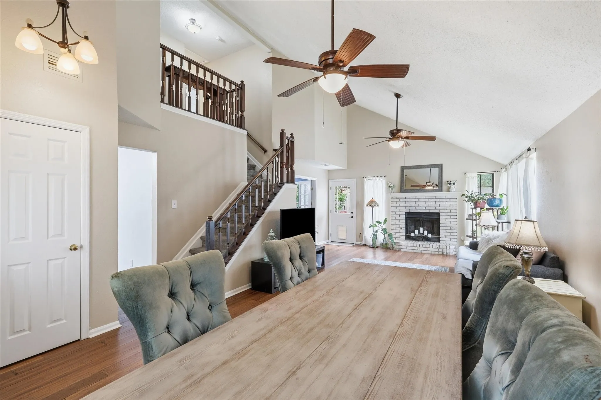 Great room featuring vaulted ceilings, wood-finish flooring, a white brick fireplace, multiple ceiling fans, and a second-story interior balcony