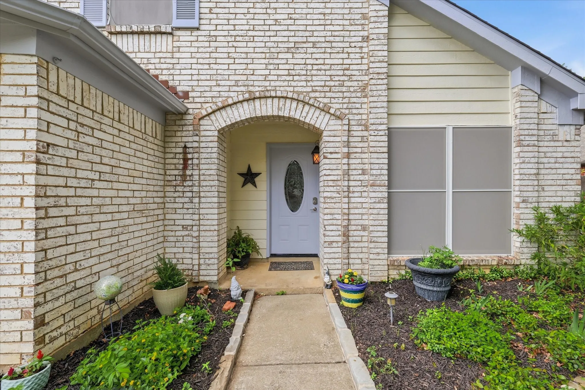Brick exterior featuring a covered arched entryway with a paneled door, a large window with white framing, and mature landscaping