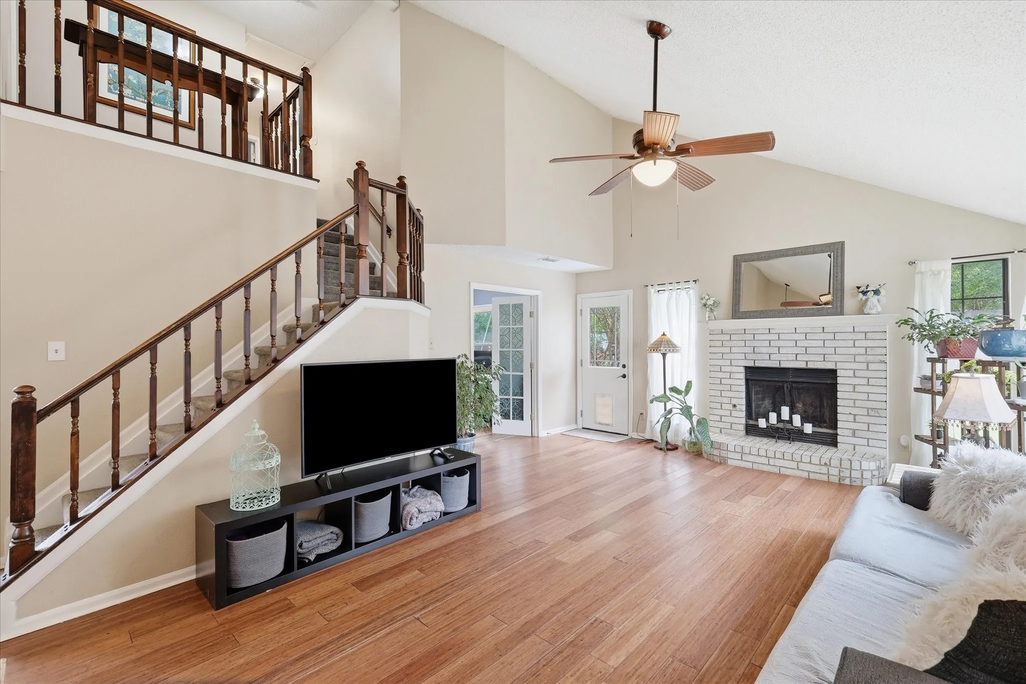 Spacious living area featuring wood-finish flooring, a white brick fireplace with a hearth, and a vaulted ceiling with a ceiling fan