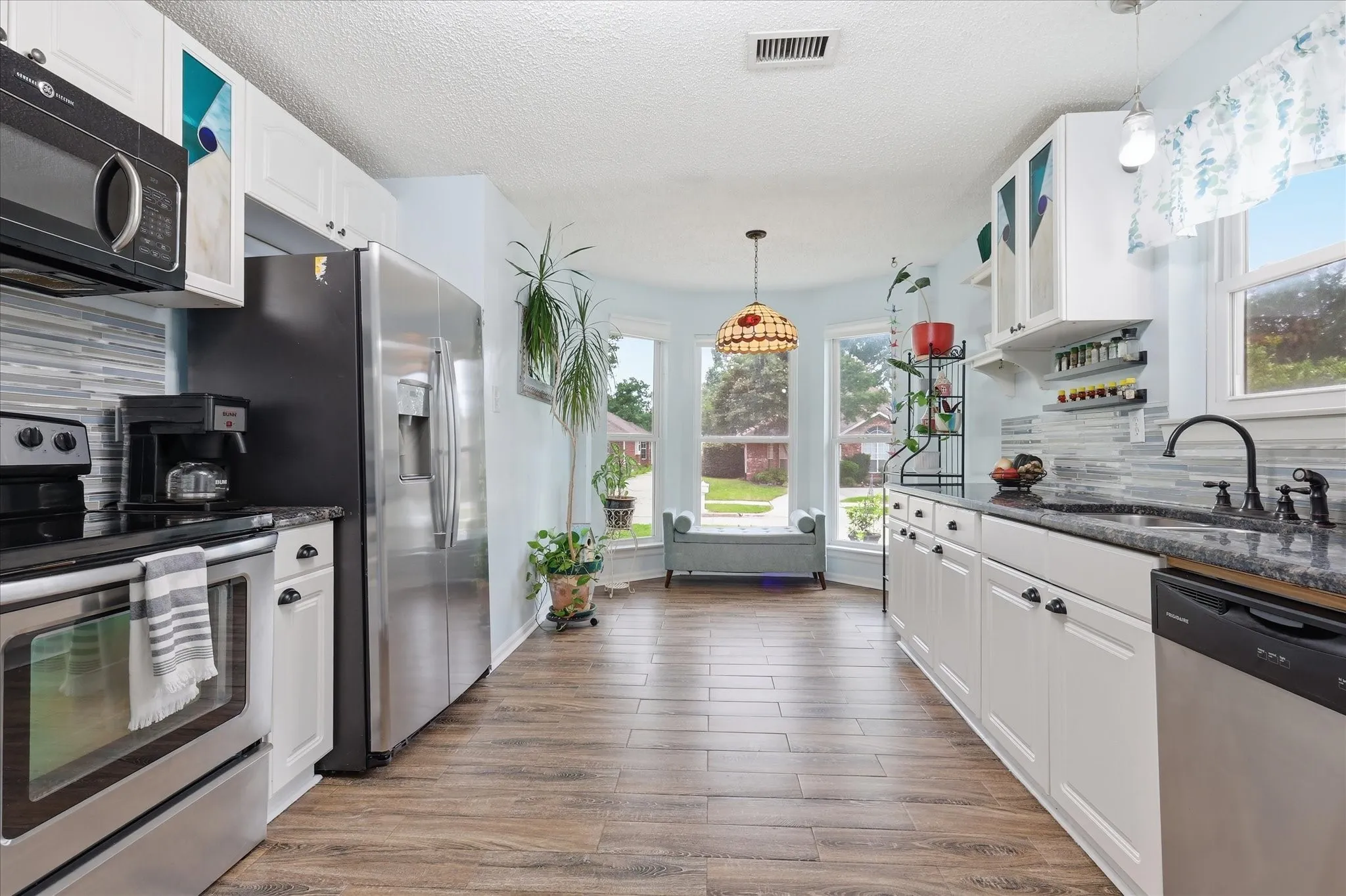 Bright kitchen featuring wood-finish flooring, white cabinetry, and a bay window