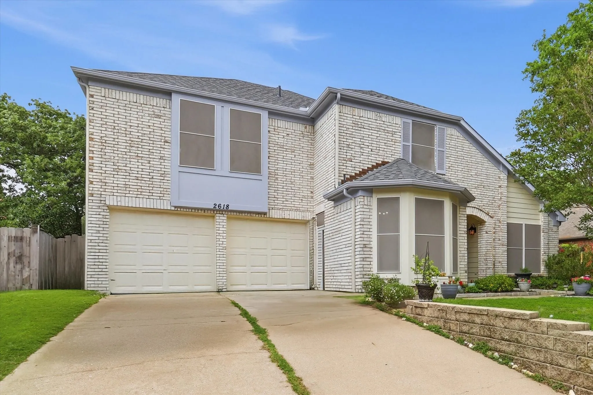 Two-story residence featuring a light-colored brick exterior, a two-car garage, and a concrete driveway