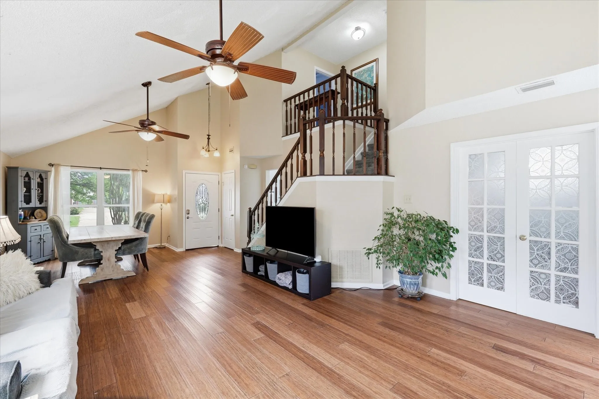 Open-concept living area featuring wood-finish flooring, vaulted ceilings, and a wooden baluster staircase
