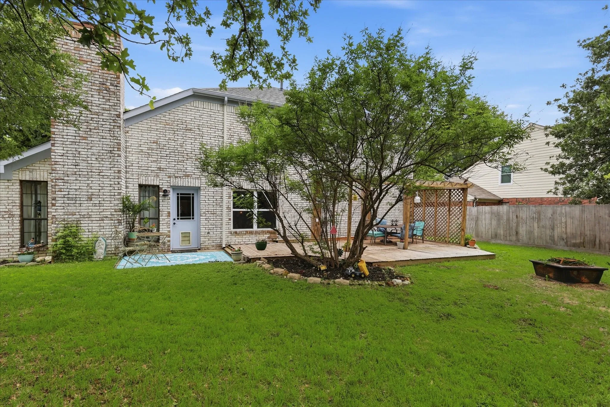 Expansive backyard featuring a brick exterior, a wooden deck, a pergola, and mature trees