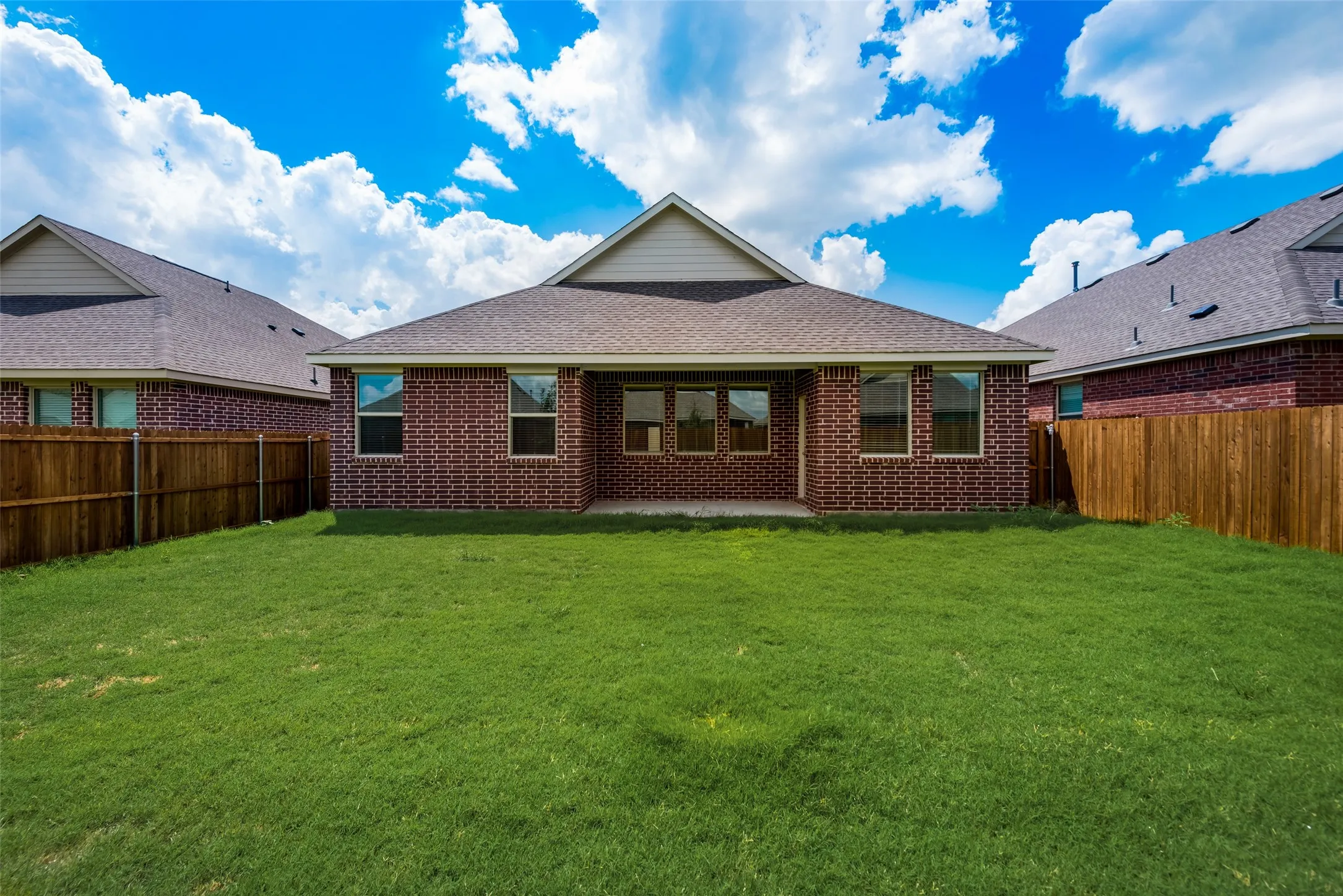 Expansive backyard featuring a lush lawn, a full brick exterior, a covered concrete patio, a shingle roof, and a wood privacy fence