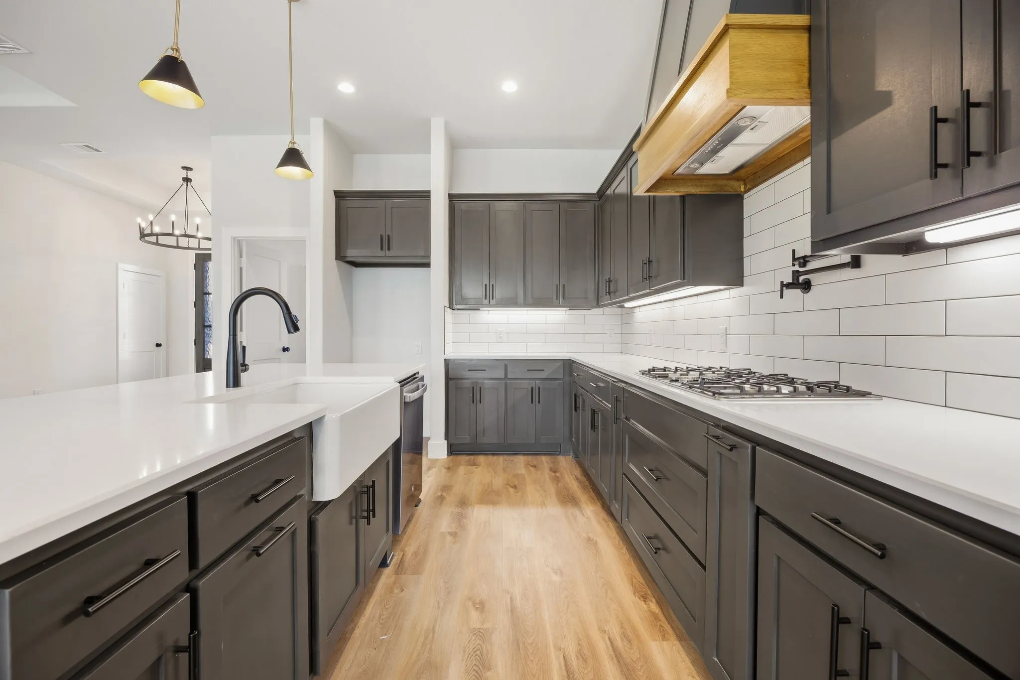 Kitchen featuring a farmhouse sink, gas range, wood-finish flooring, dark cabinetry, and white countertops