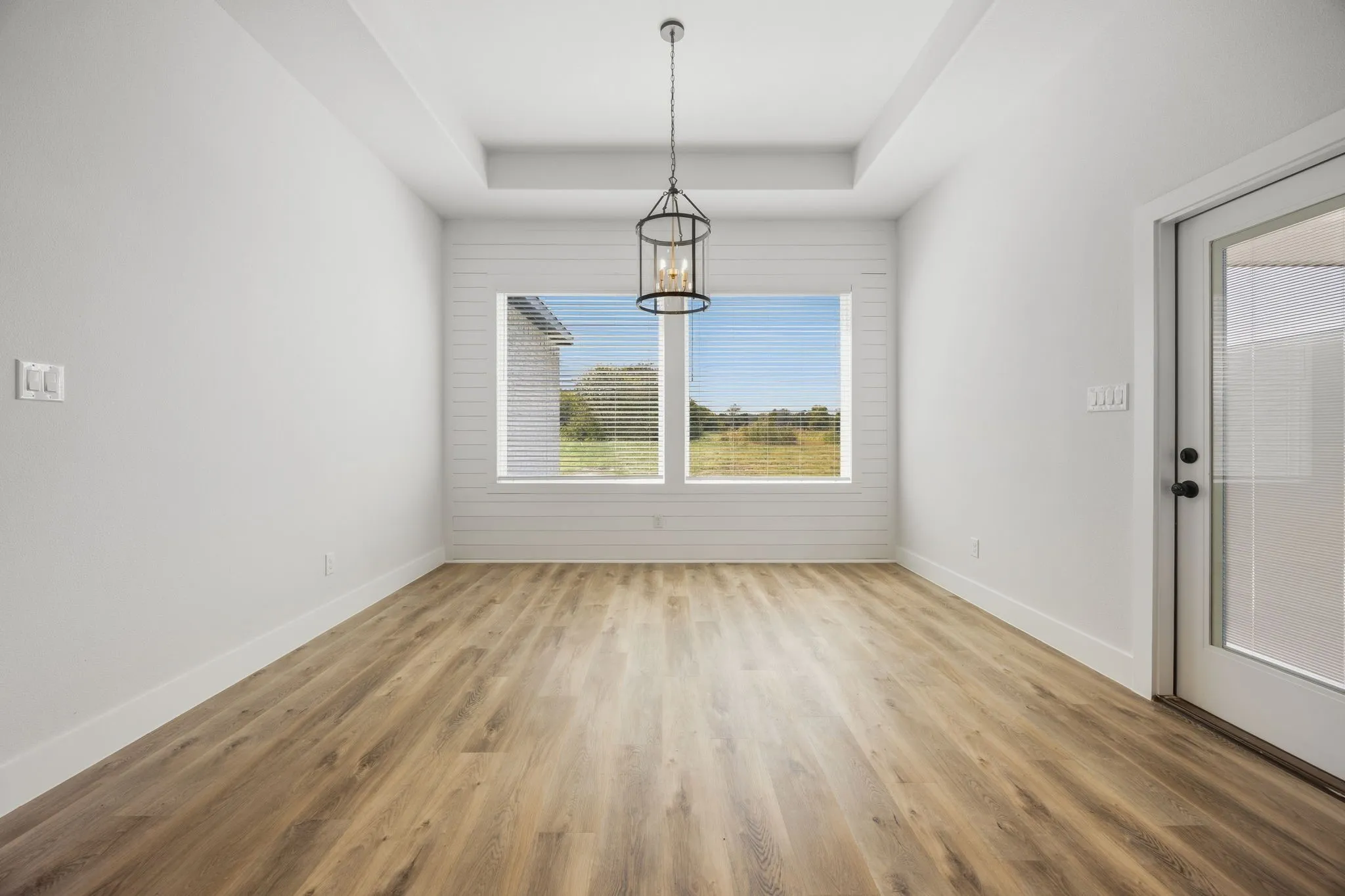 Tray ceiling with a decorative pendant light fixture, wood-finish flooring, and white shiplap accent wall