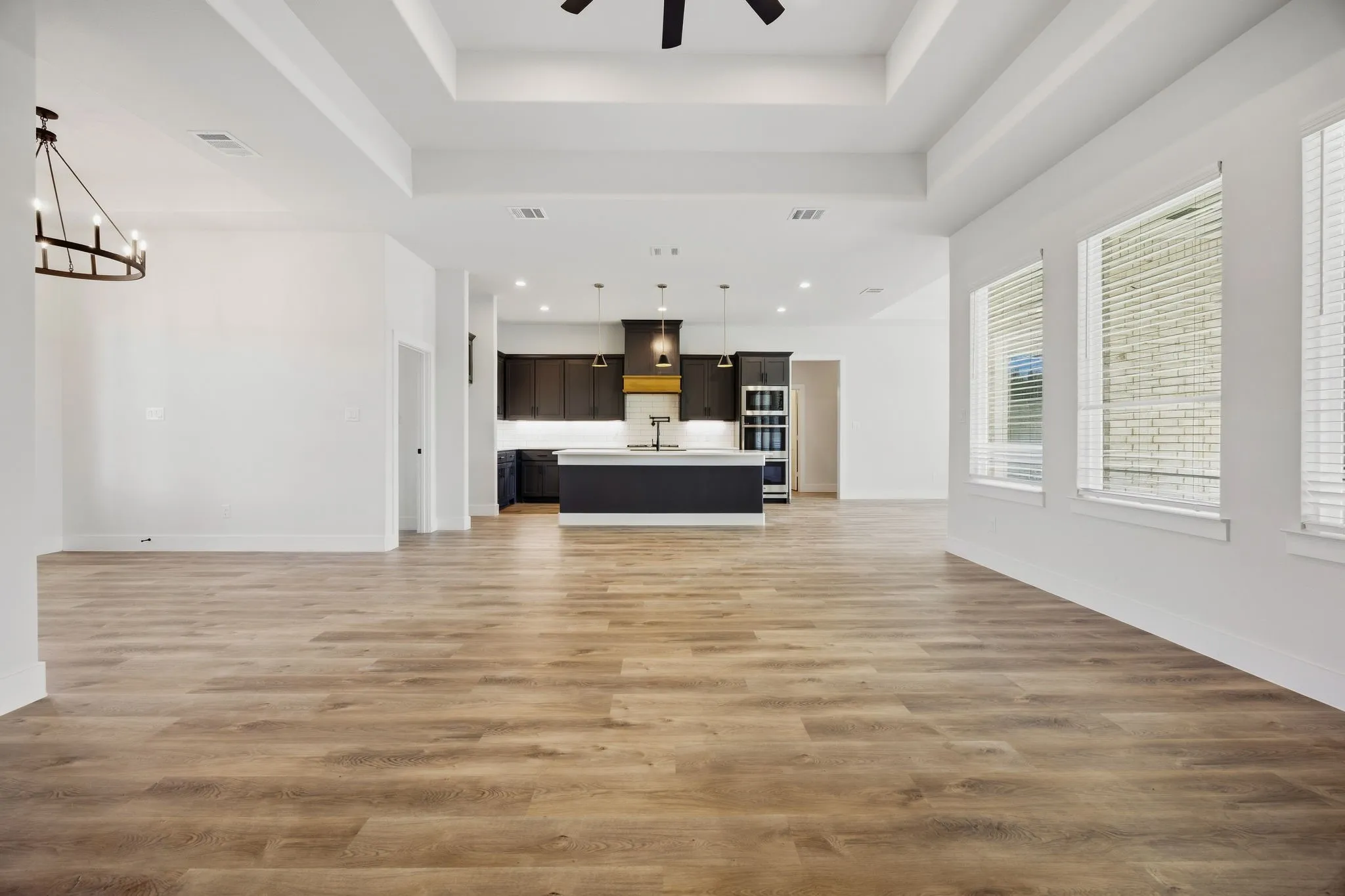 Expansive room with wood-finish flooring, tray ceilings, and an open layout to the kitchen