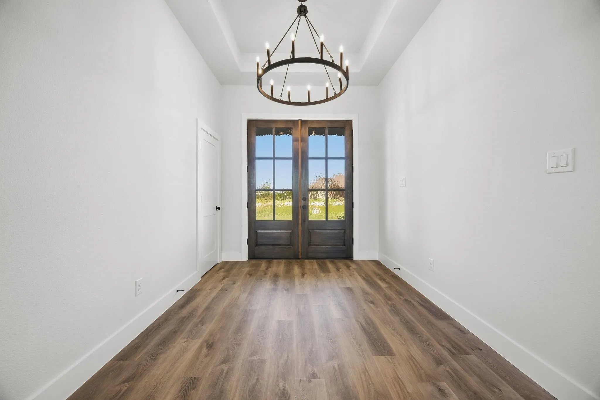 Double entry doors with glass panels, wood-finish flooring, tray ceiling, and a large circular chandelier