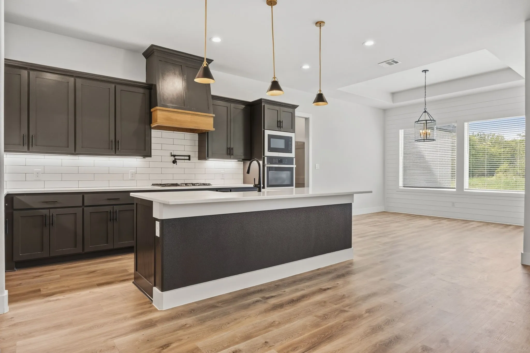 Contemporary kitchen featuring dark cabinetry, white subway tile backsplash, white countertops, a central island, and wood-finish flooring